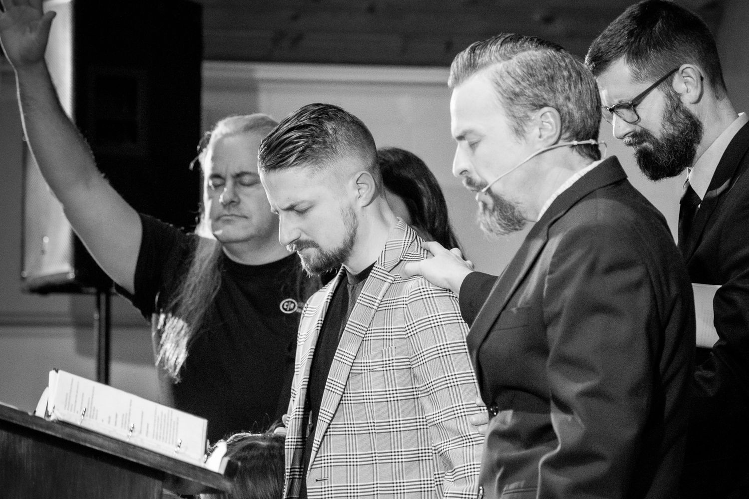black and white image of all four pastors praying together on the stage at Crossroads Morgantown at Pastor Brandon's pastoral commissioning