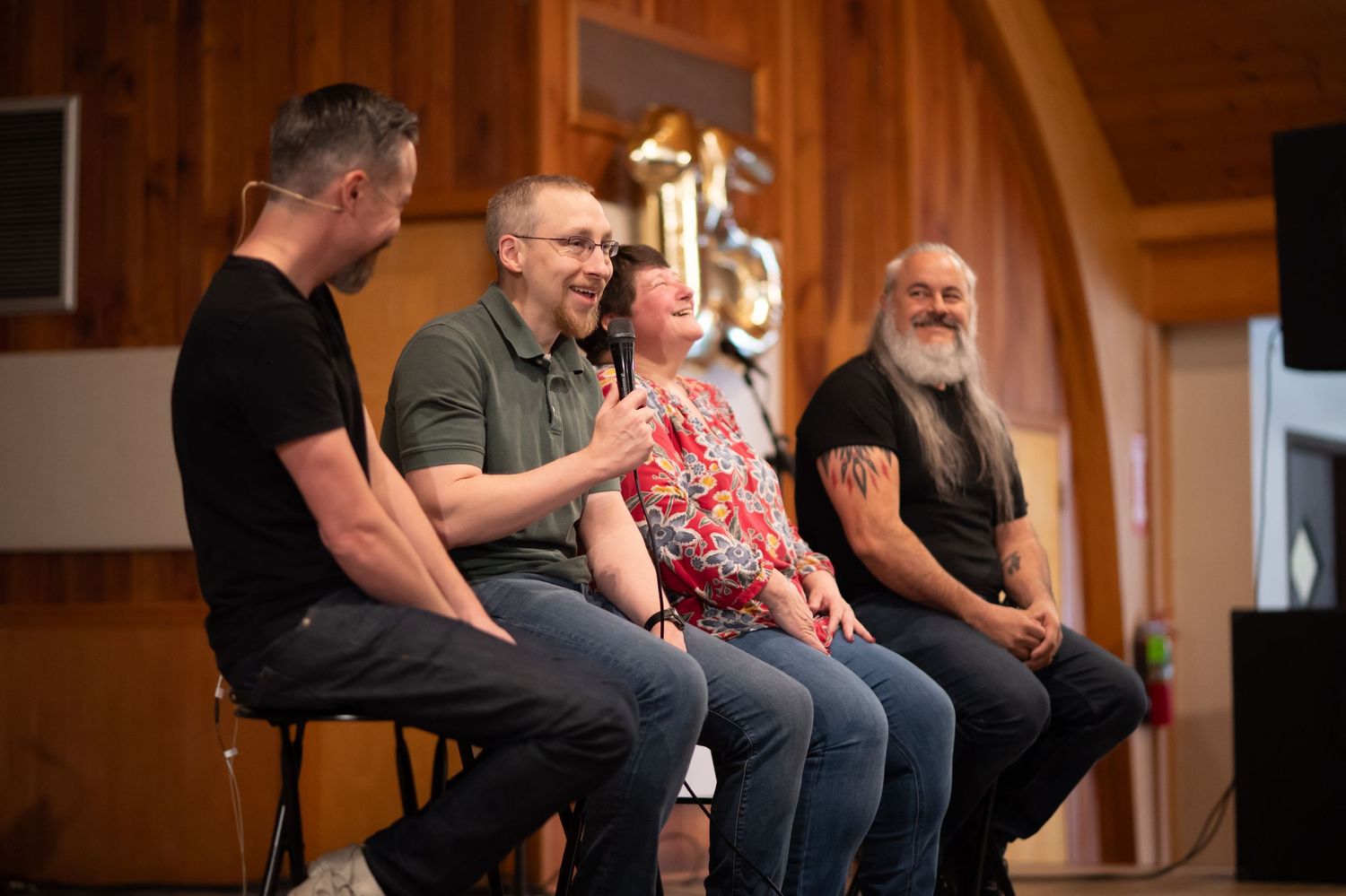 two church members sit on folding chairs on the stage at Crossroads Morgantown with two pastors, laughing at something one of them said