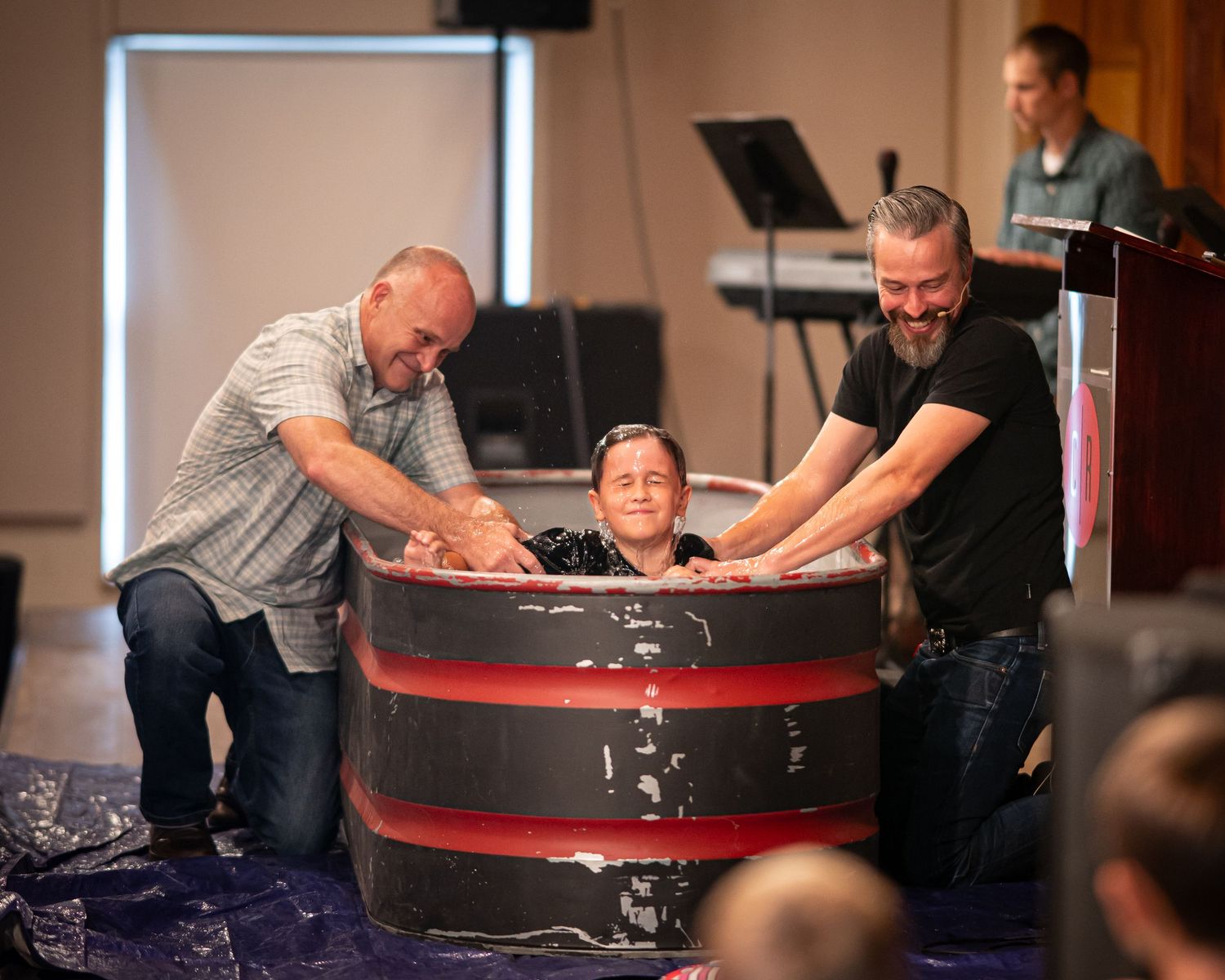 a young boy sits in a baptismal on stage at Crossroads Morgantown during Sunday service, with his father and Pastor Chris on either side