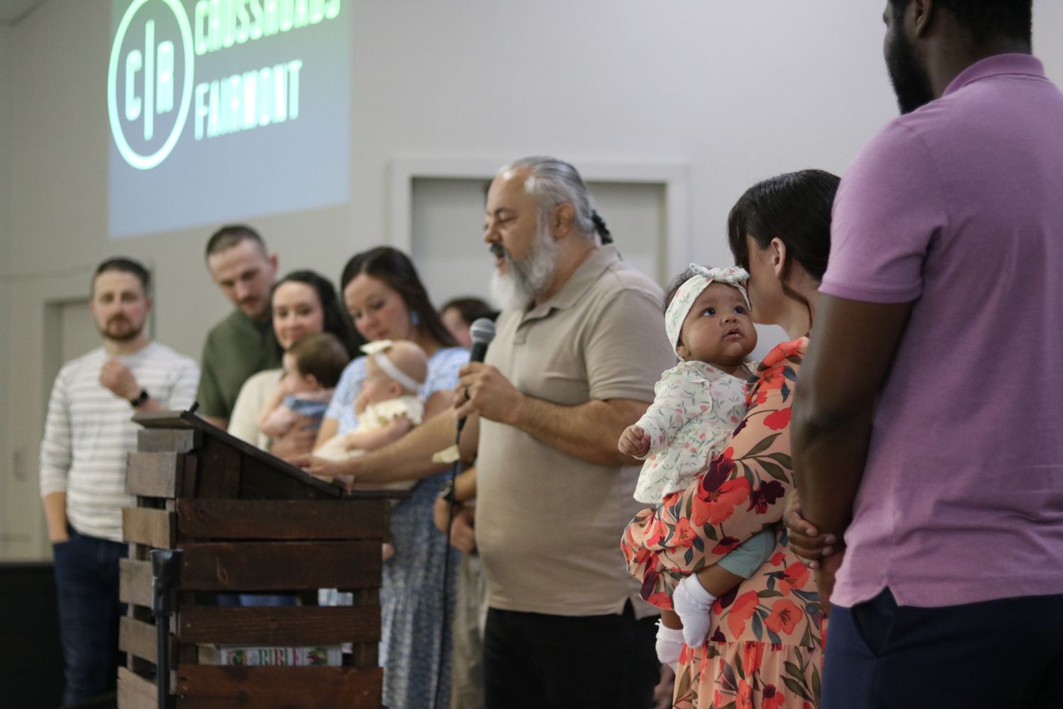 Pastor Chatto stands on the stage at Crossroads Fairmont surrounded by parents with their babies during a baby dedication at Sunday service