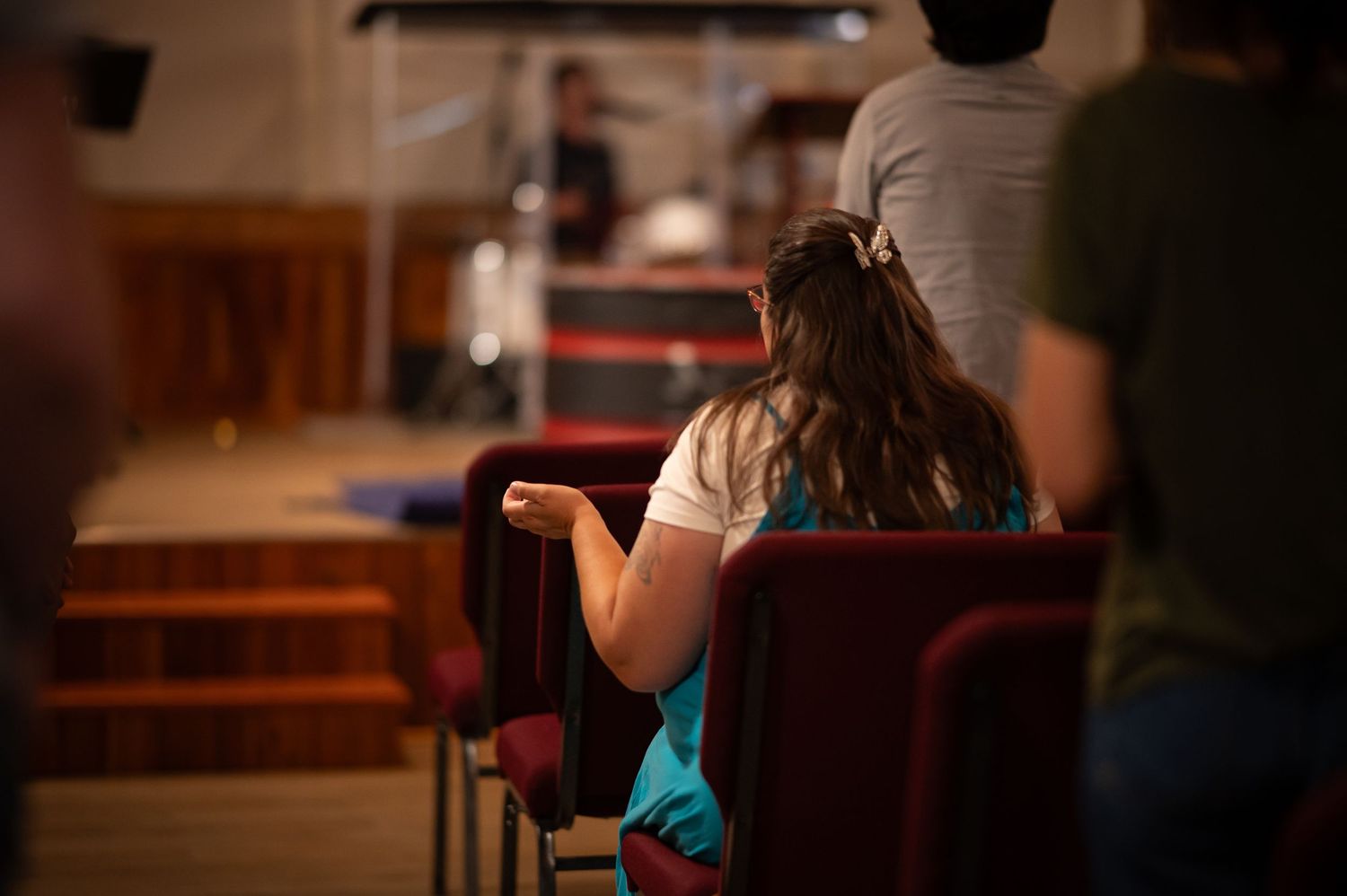 a woman sits in the seats at Crossroads Morgantown, a hand lifted in worship as the worship team leads a song during Sunday service.