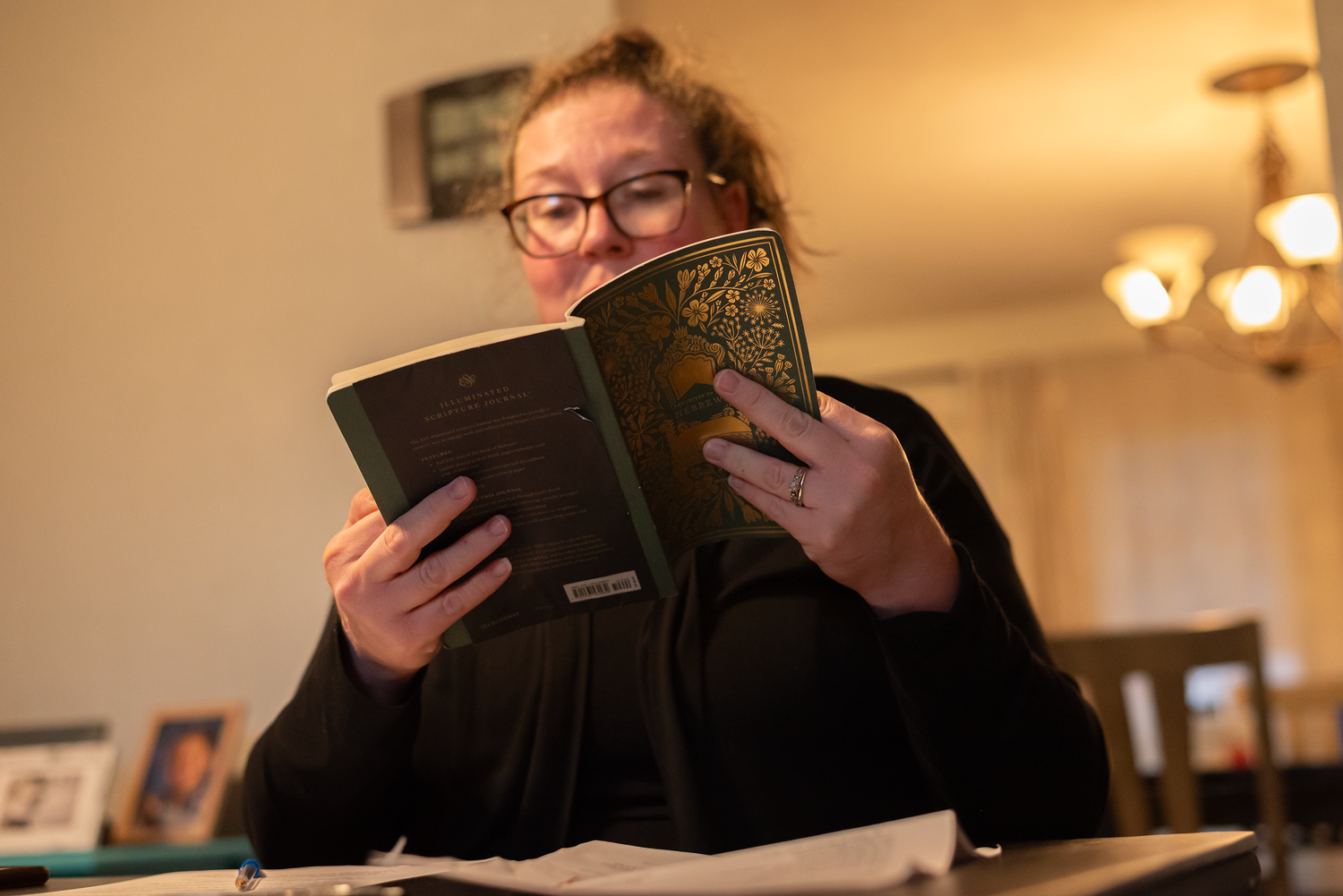 a woman holds an open devotional book and reads from it during a community group meeting at a home in Fairmont, WV