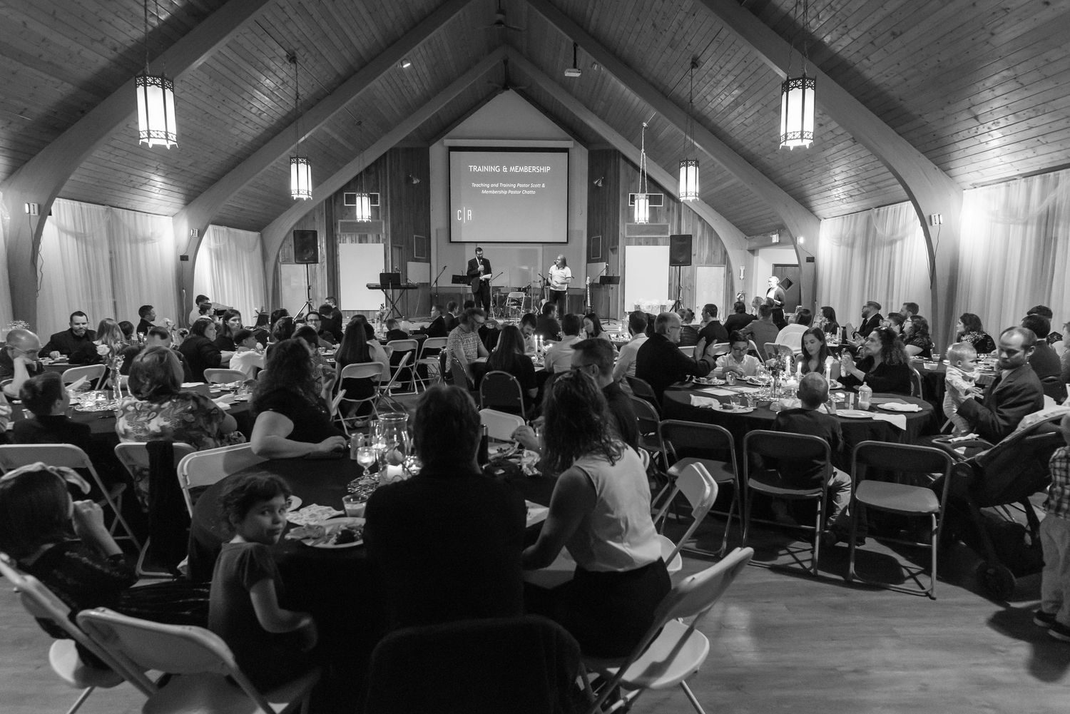 black and white image of Crossroads church members sitting around round tables in the auditorium during an event at Crossroads Morgantown