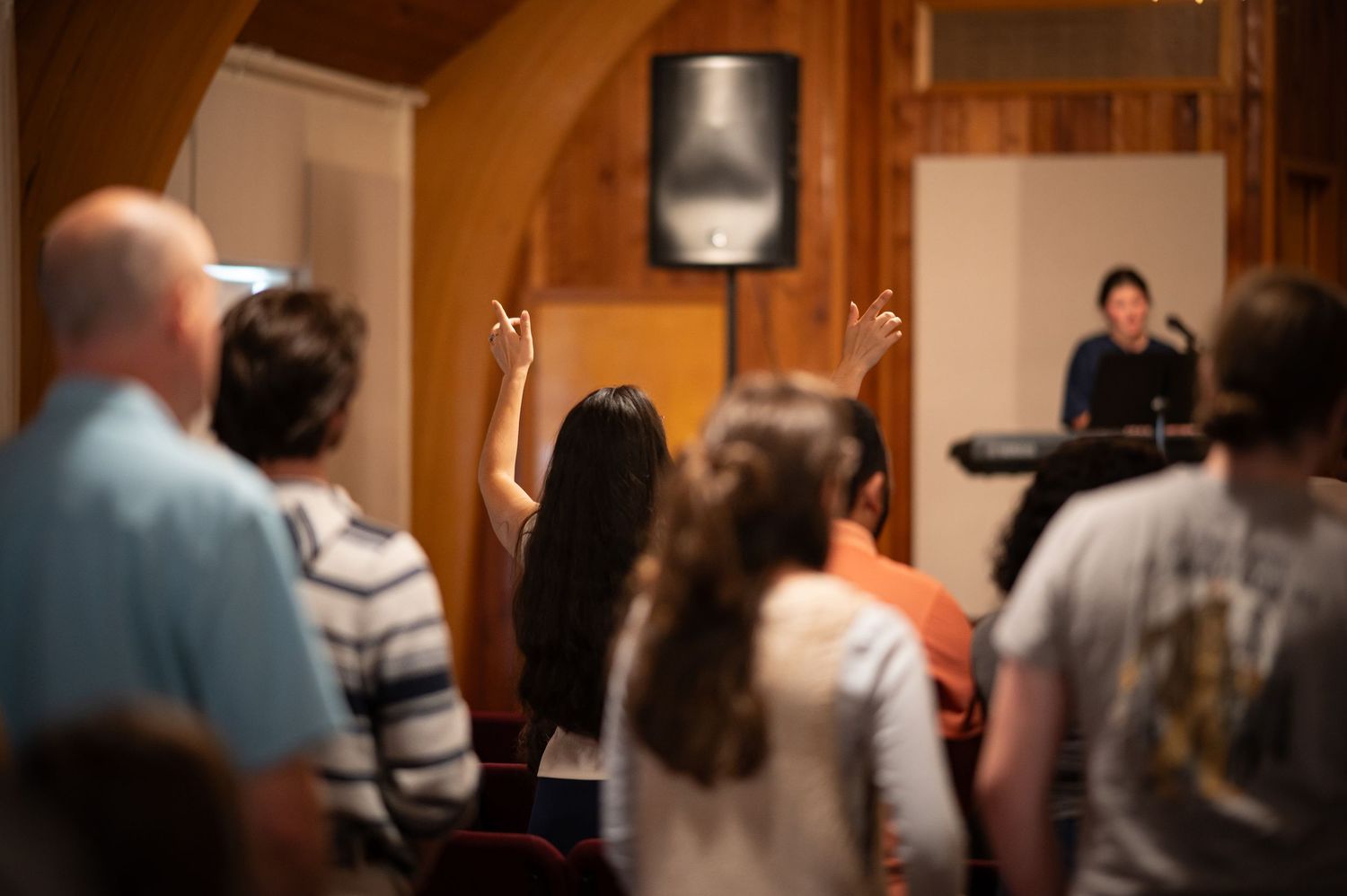 a woman stands in the auditorium during worship service at Crossroads, singing with hands raised, with the worship team in the background
