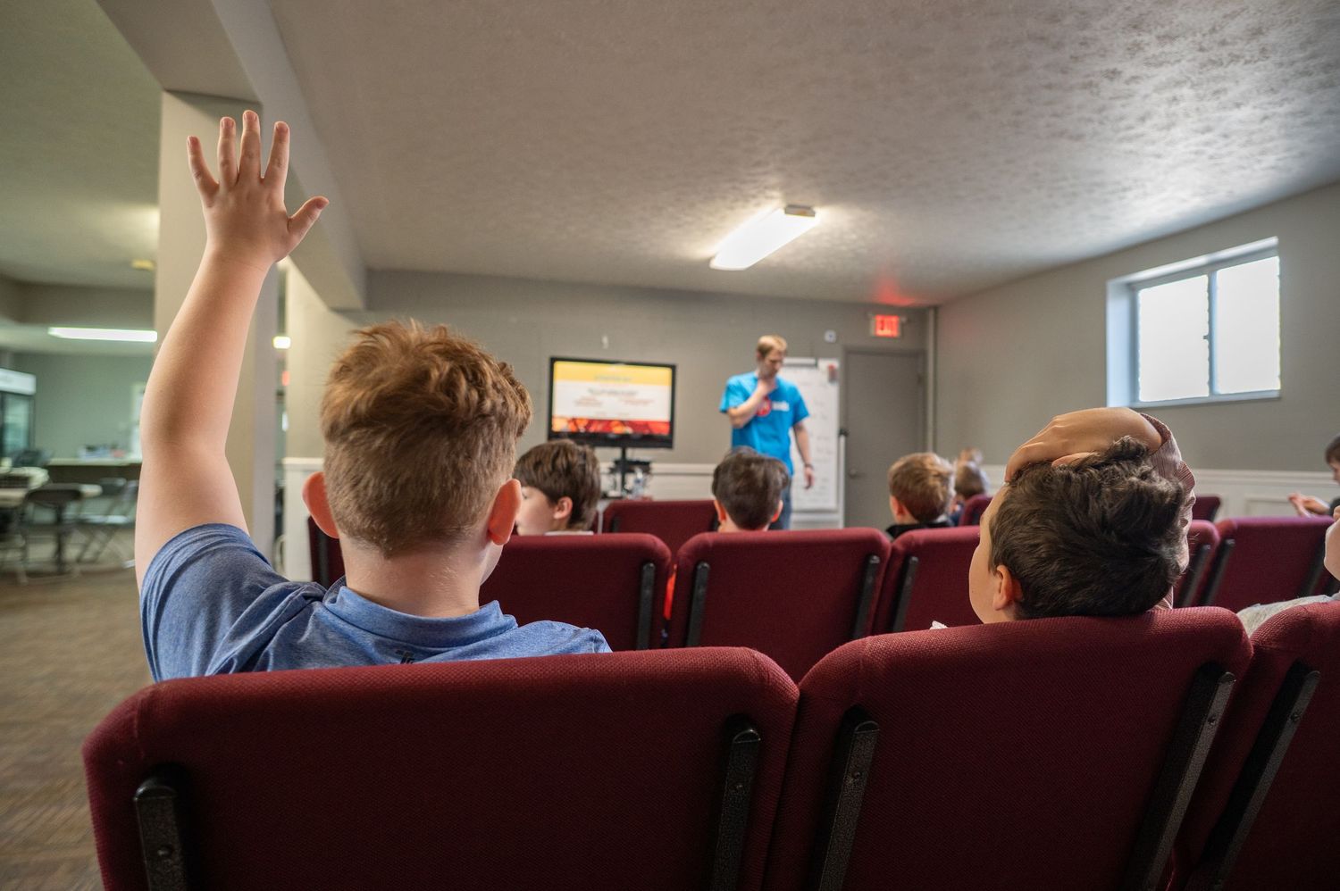 view from behind a classroom as a young boy raises his hand to answer a question during children's church at Crossroads Morgantown