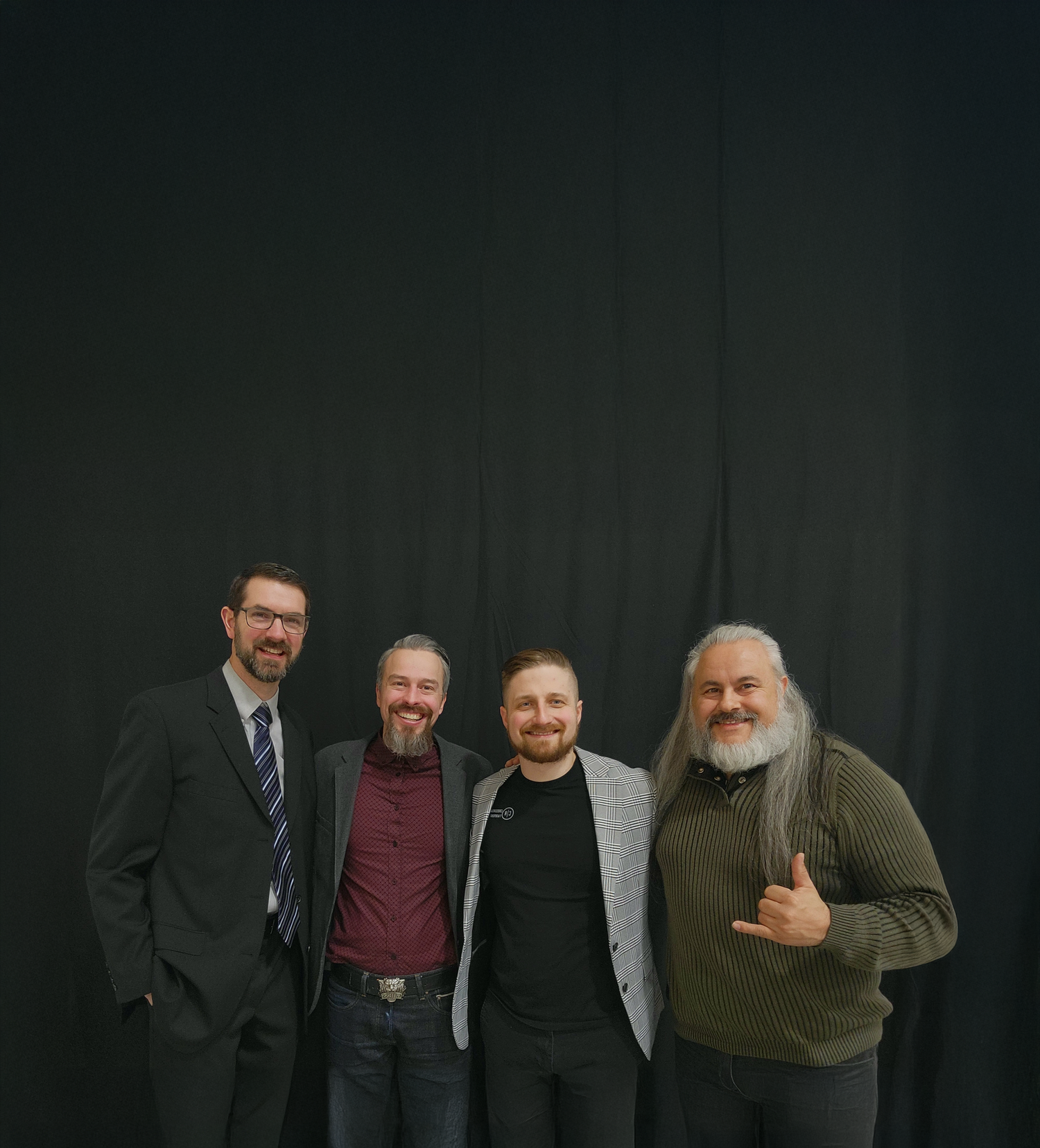 all four Crossroads Church pastors stand together, smiling, in front of a dark green curtain and pose for a portrait during a church event