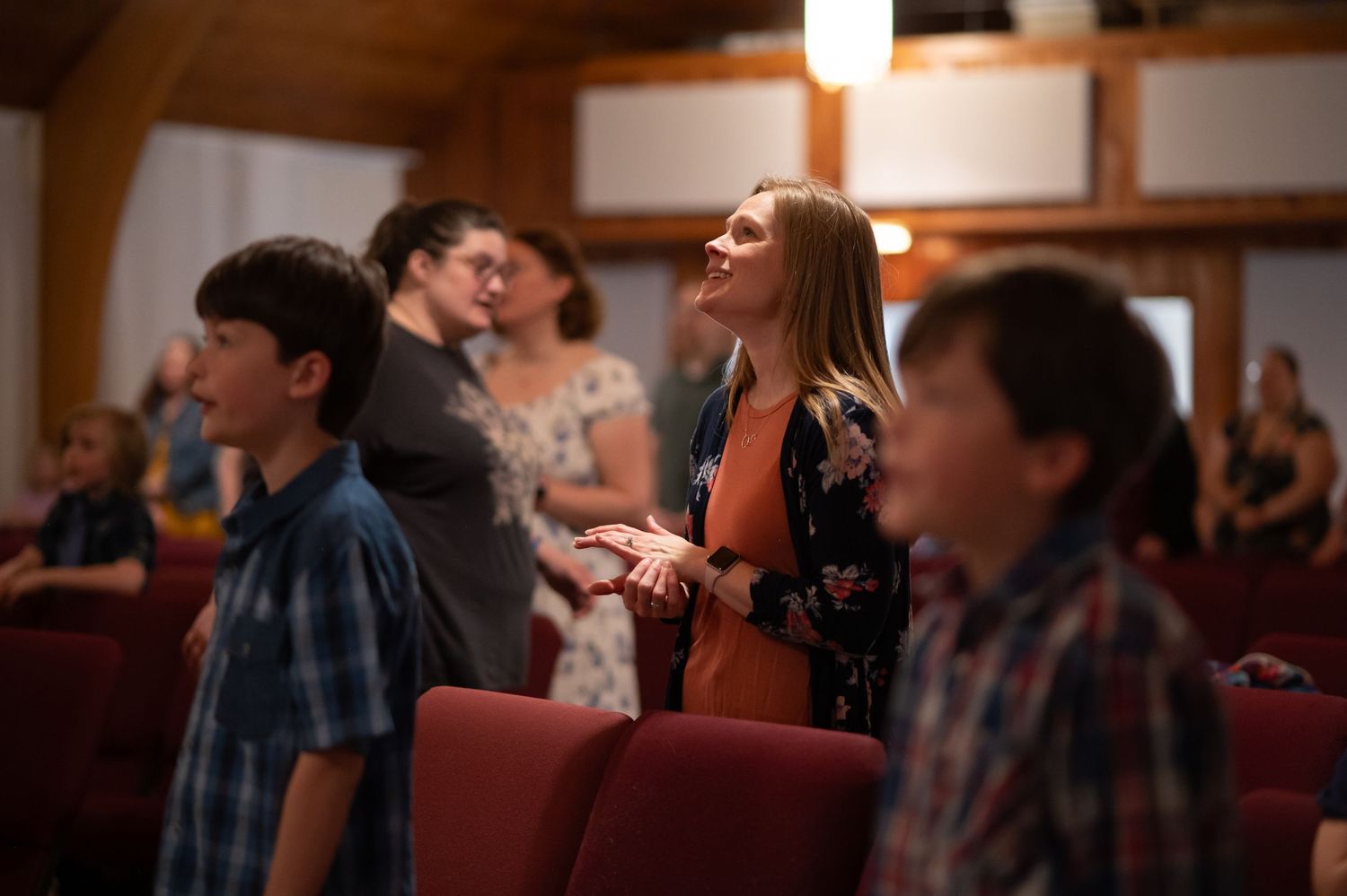 a woman stands in the seats during a church service at Crossroads Morgantown, singing and clapping with her hands raised