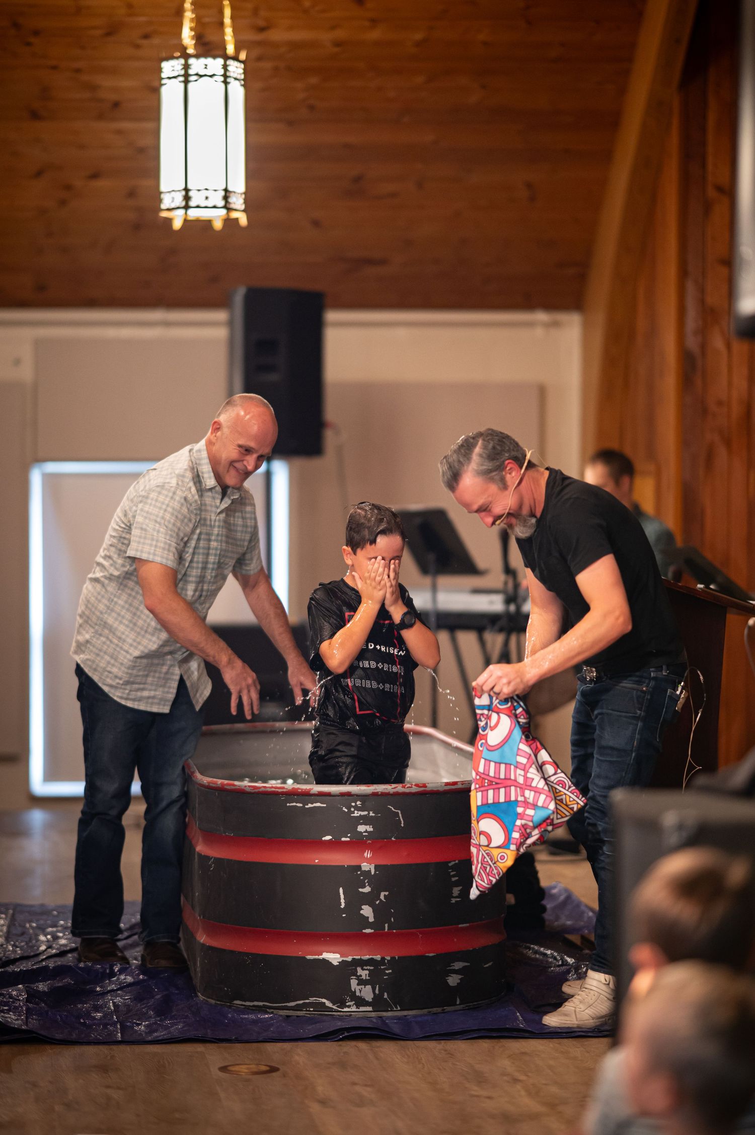 Pastor Chris and a Crossroads member smile as they baptize the member's son in a baptismal at Crossroads Morgantown