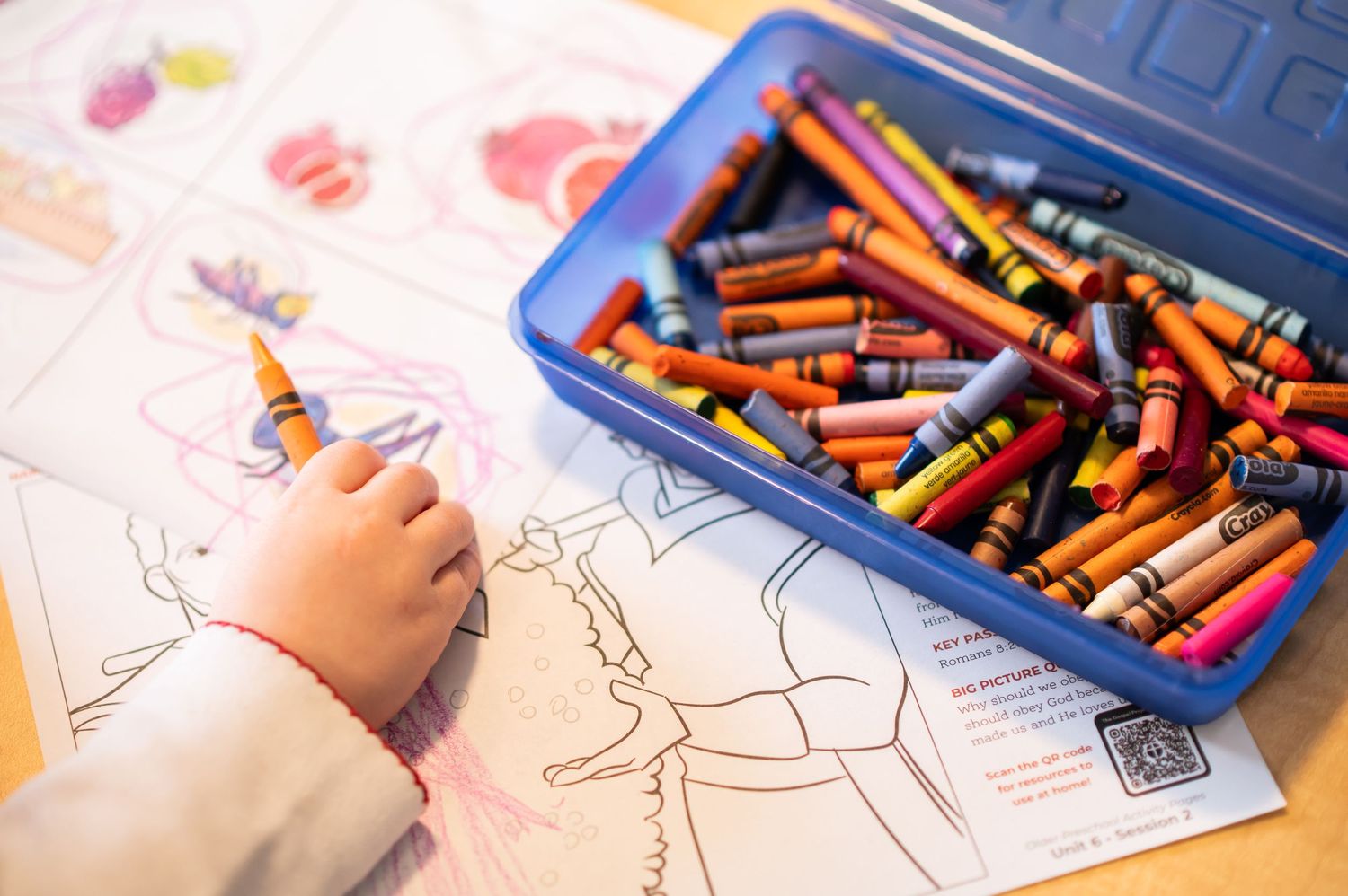 a little girl's hand holds a crayon as she colors a Sunday school coloring sheet during church service at Crossroads Church in Morgantown