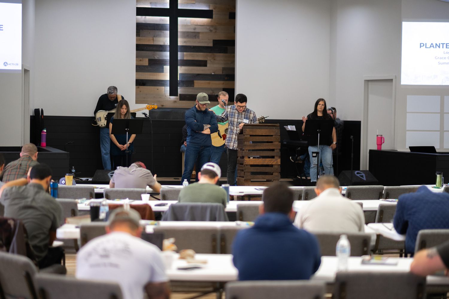 attendees at a Crossroads Church conference sit at long tables in the Crossroads Fairmont auditorium and read their conference materials