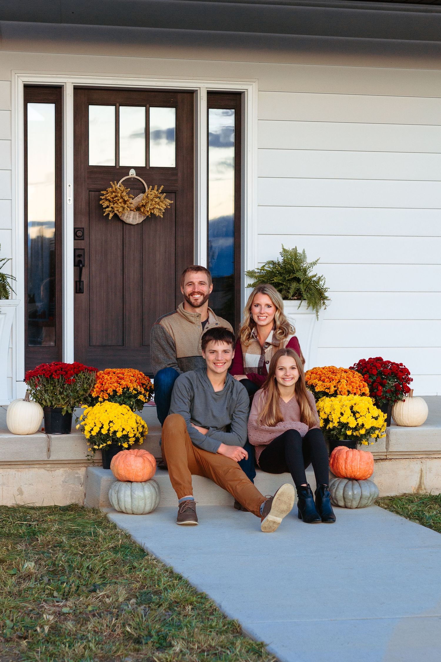 Family sitting on front porch decorated with fall mums and pumpkins.