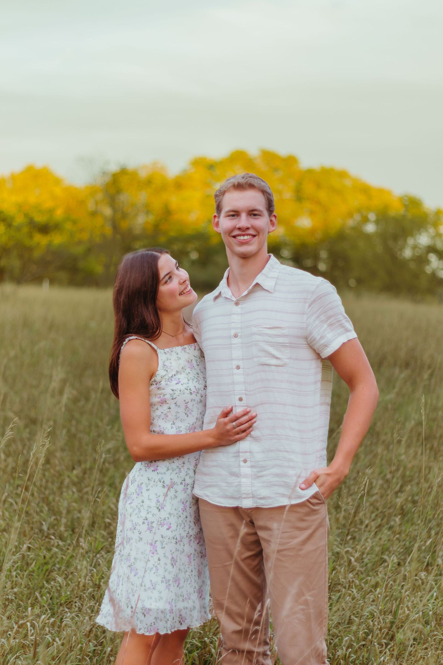 Happy couple posing in field with autumn foliage in background.