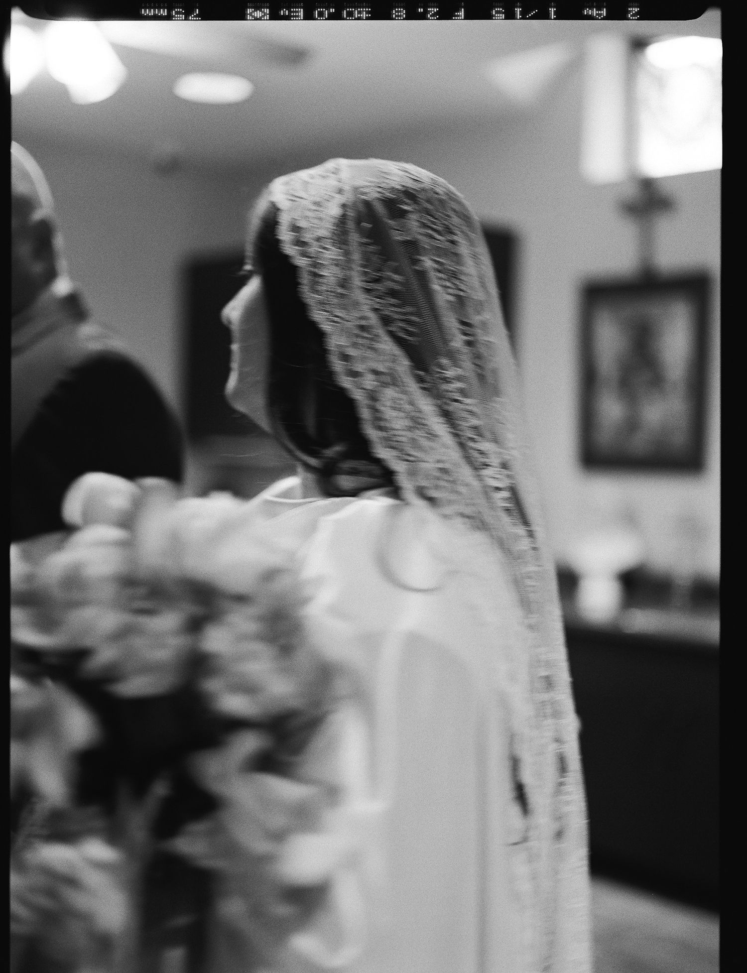 Bride wearing a lace veil holding a bouquet of white flowers in a black and white film photo looking at her dad.
