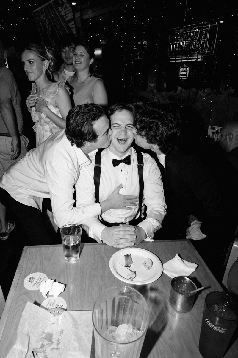 Black and white photo of laughing young man in bow tie and suspenders at a table during a formal event.