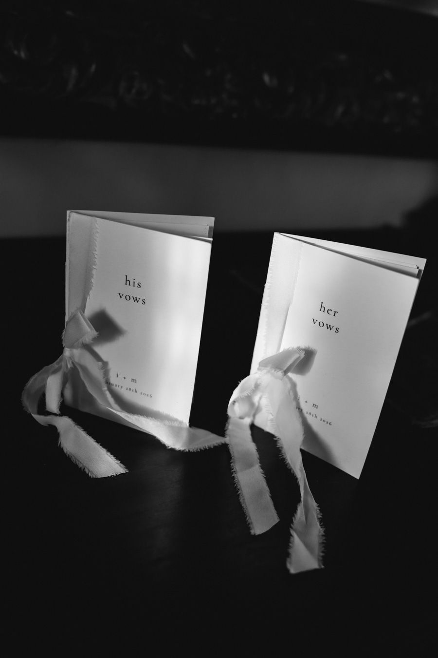 His and her vows booklets tied with ribbon bows displayed in black and white.