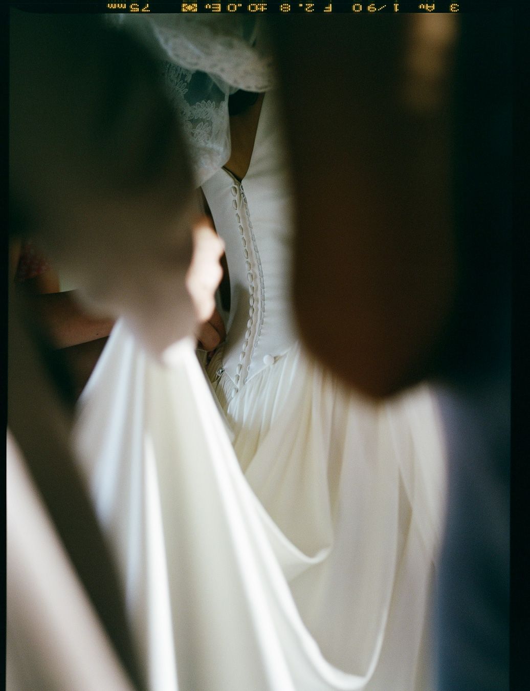 Close-up detail of wedding dress zipper being fastened by bridesmaid hands before ceremony.