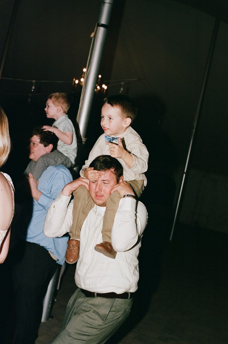 A man carries a young boy on his shoulders at an indoor event, covering his eyes playfully.