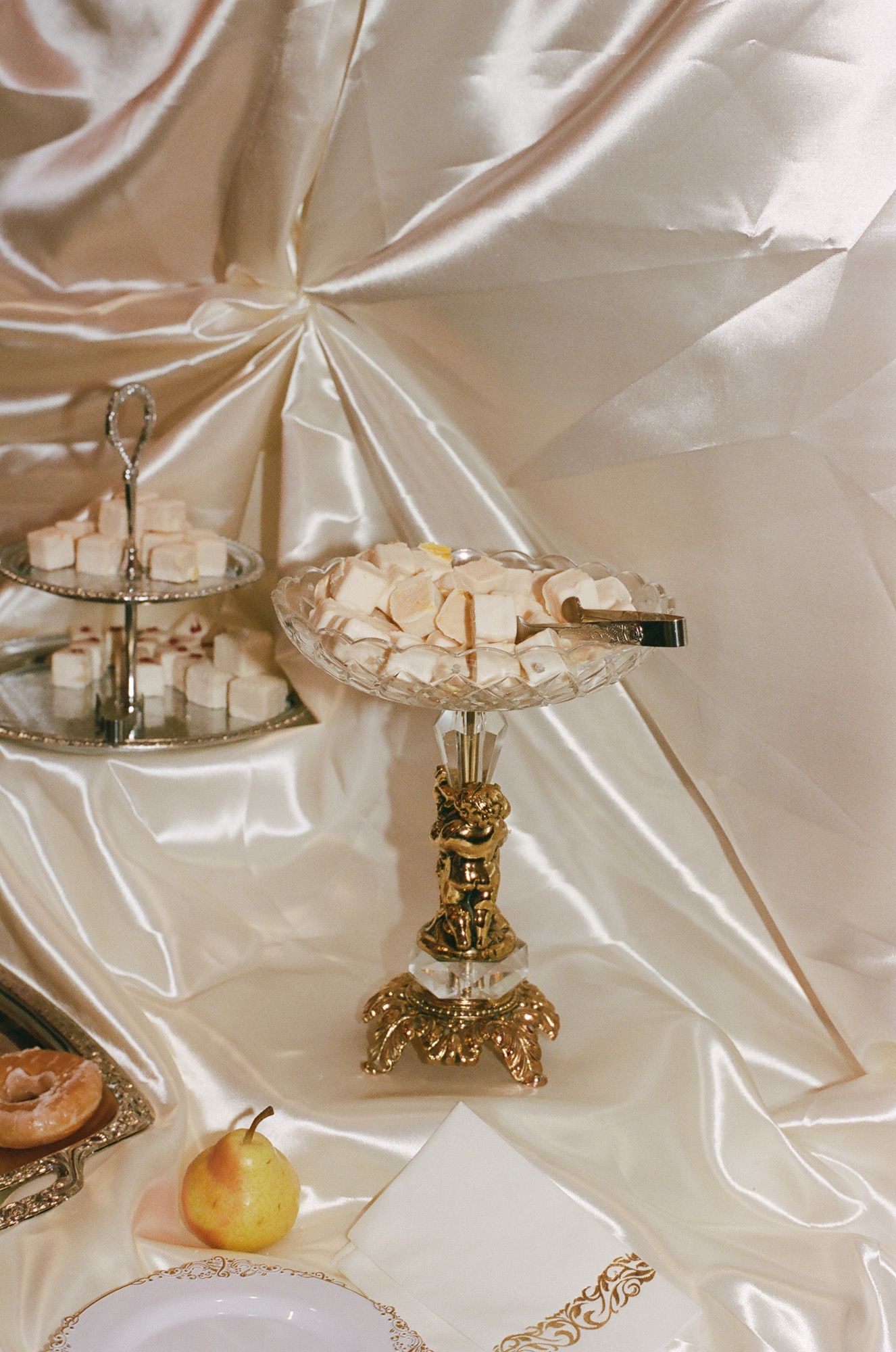Ornate gold pedestal dish filled with white sugar cubes on a satin-draped wedding dessert table.