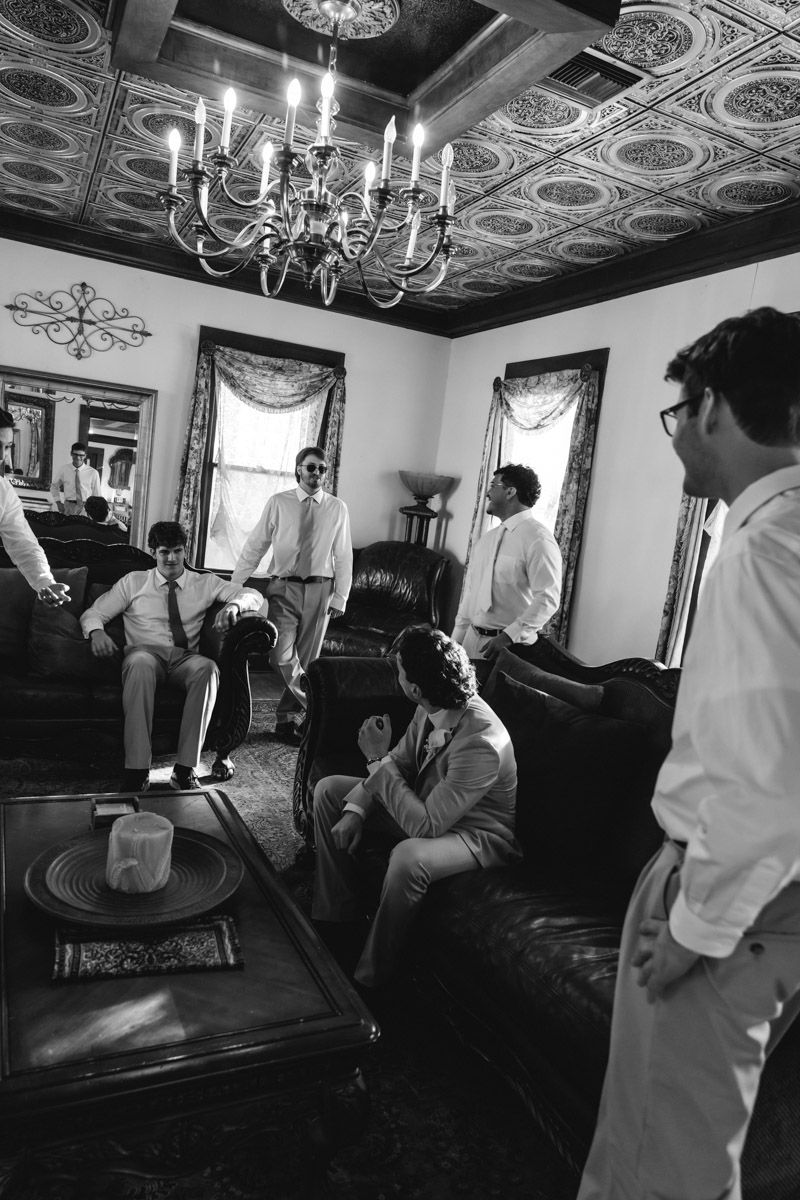 Groomsmen relaxing in an elegant room with chandelier before wedding ceremony, black and white photo.