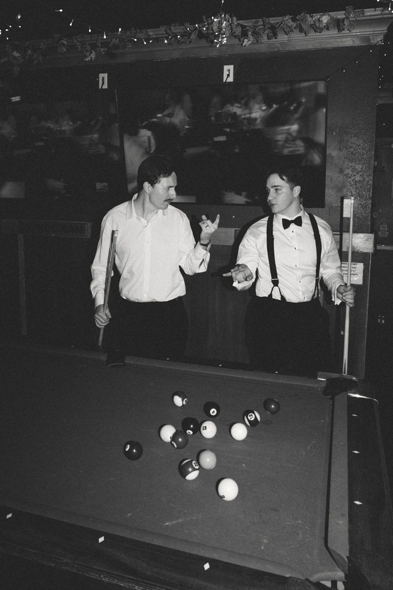 Two men in formal attire playing pool billiards, black and white photo.
