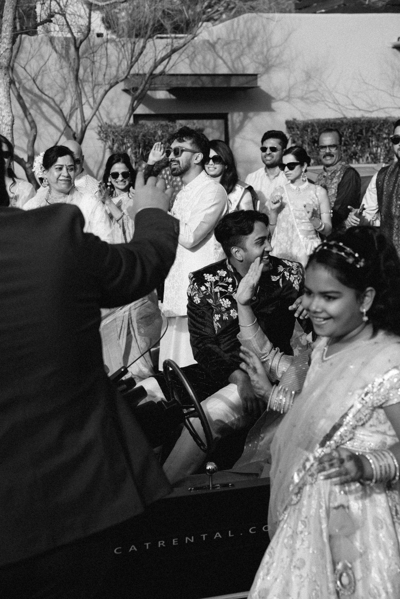 Black and white photo of wedding guests in traditional Indian clothing celebrating during a baraat procession.