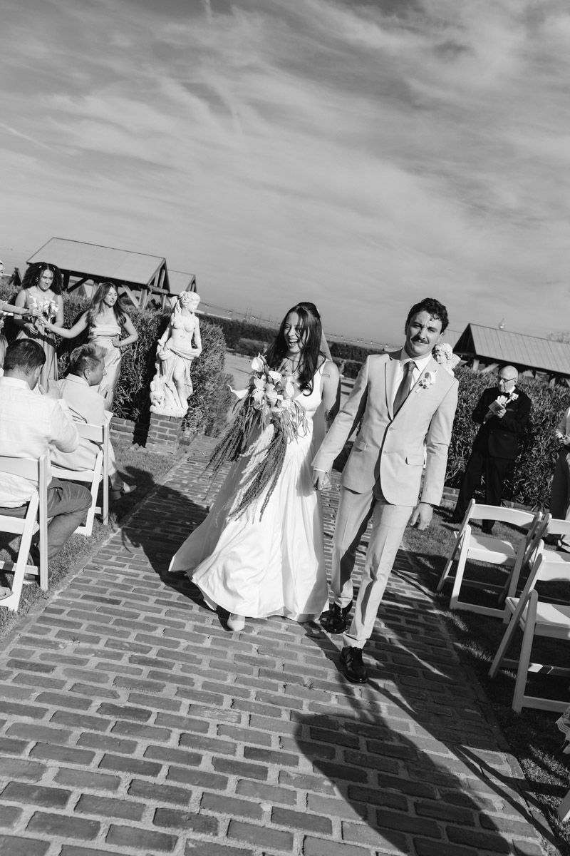 Black and white photo of a bride and groom walking back down the aisle after getting married at an outdoor wedding ceremony.