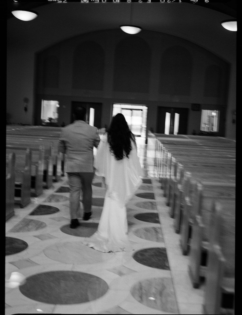 Black and white photo of a bride and groom walking down the aisle of a church after their wedding ceremony.