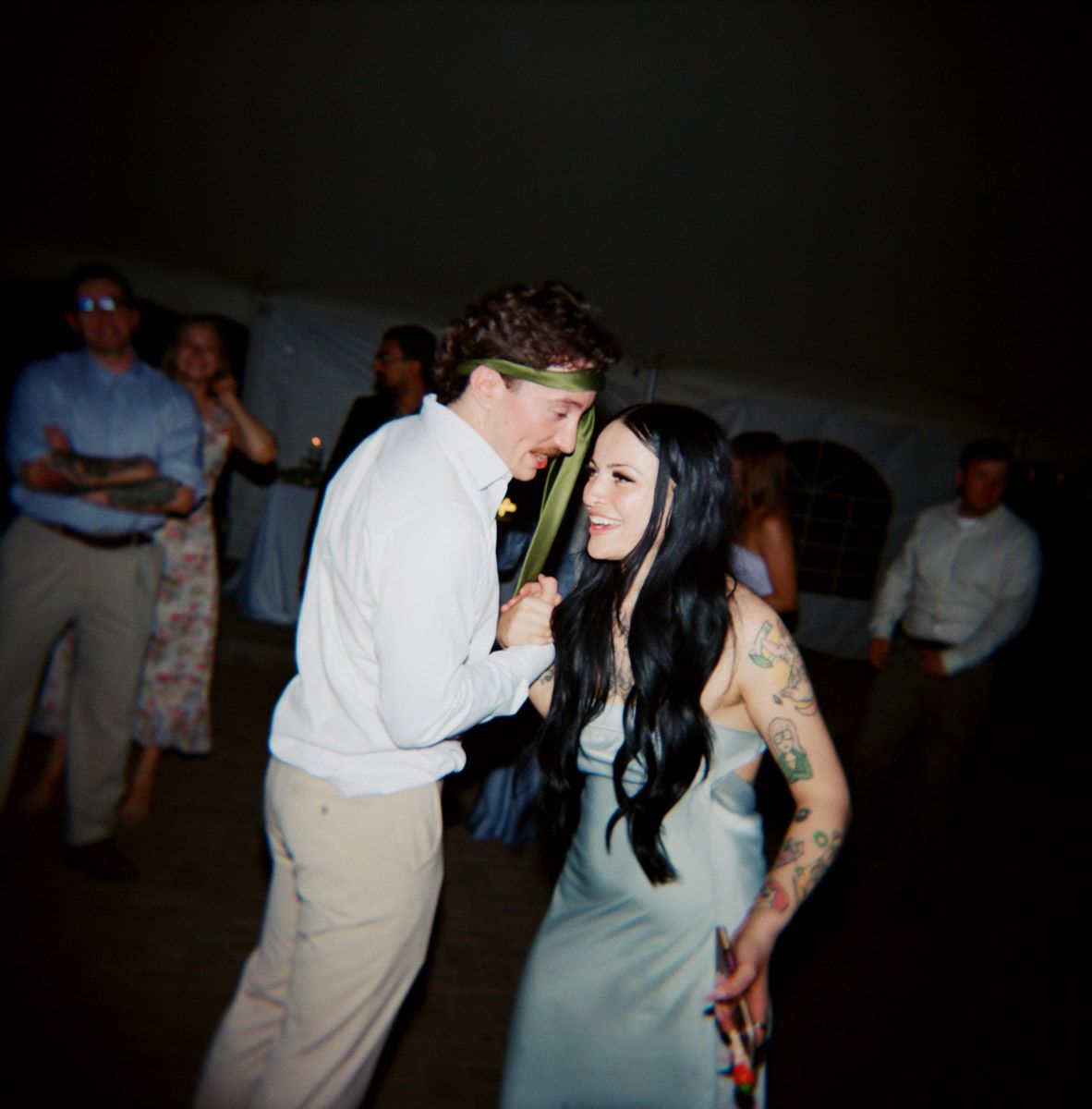 Groom and sister dance at a wedding reception, woman with tattoos in blue dress, man in white shirt.