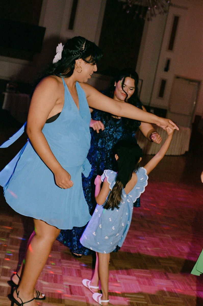 Woman and young girl dance joyfully at a wedding reception on a colorful dance floor.