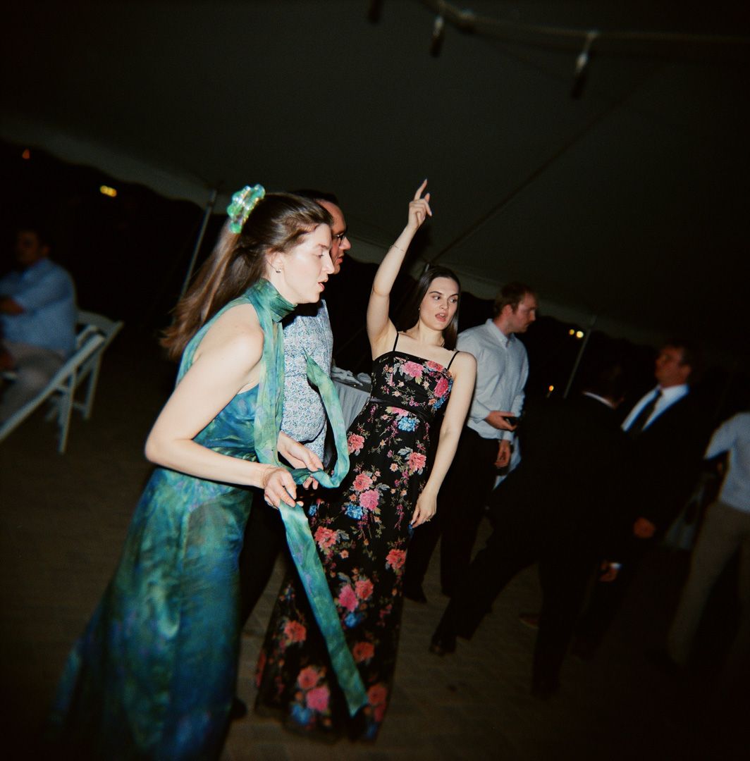 Film photo of two women dancing at outdoor wedding reception, one wearing floral dress with arm raised, and another in a green blue dress.