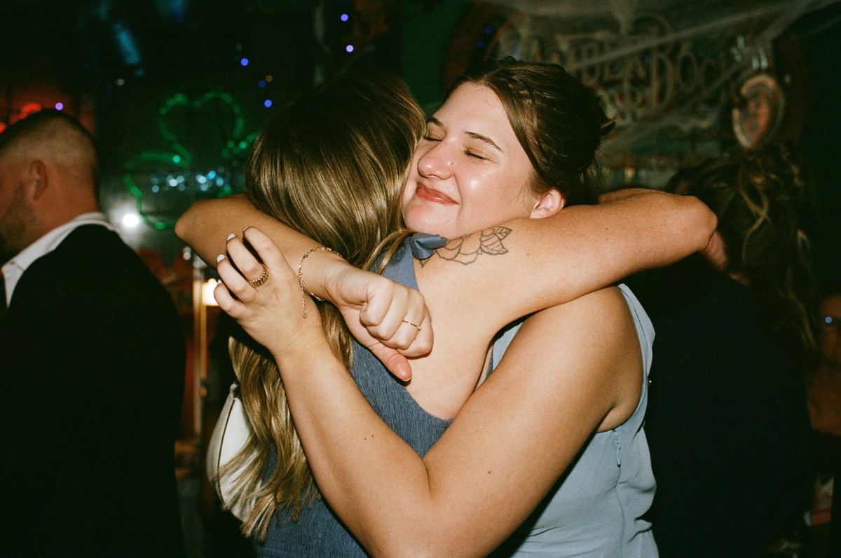 Two women sharing a warm embrace and smiling at a festive evening event.