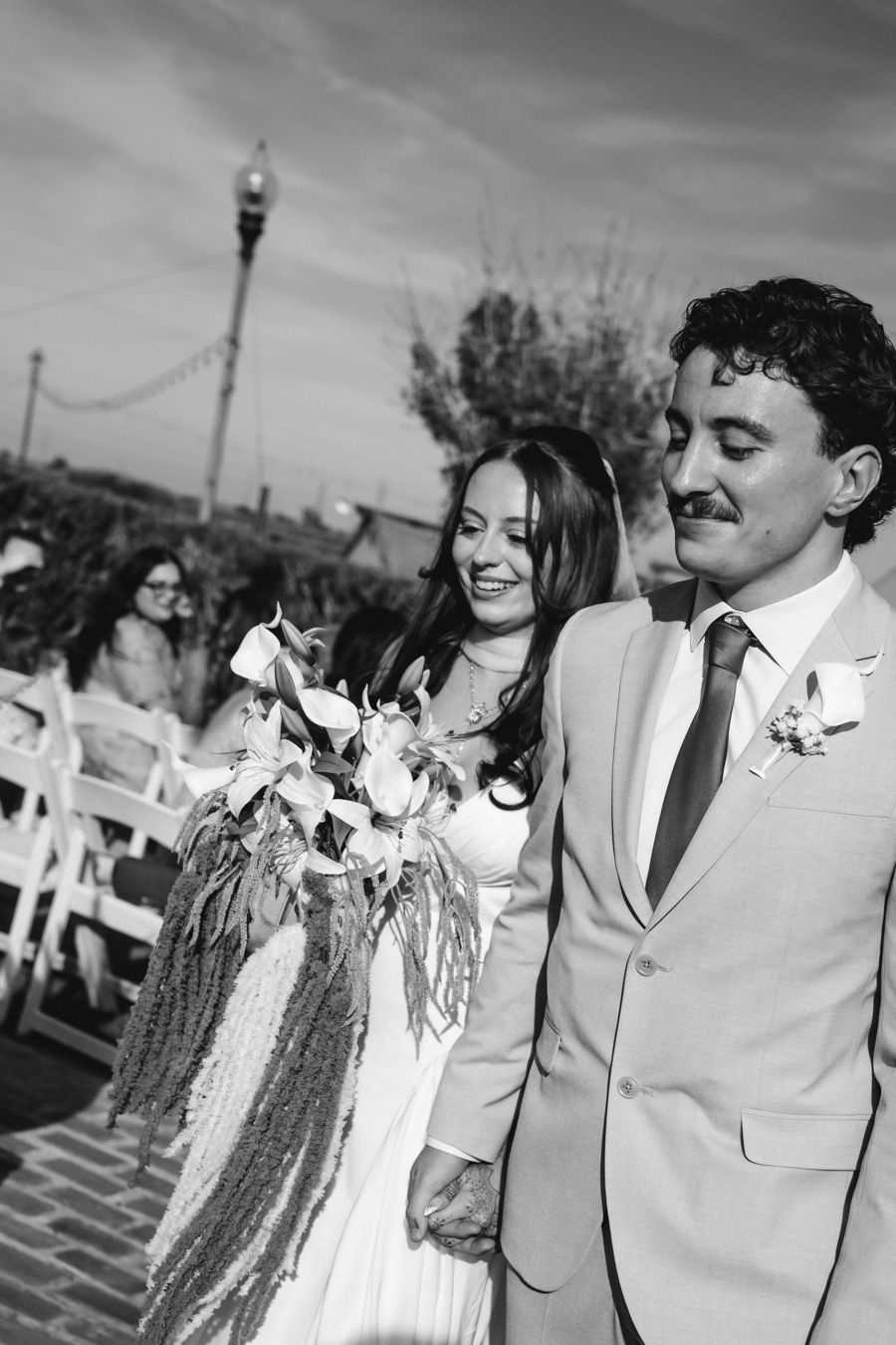 Smiling bride with bouquet and groom walk back down aisle at outdoor wedding ceremony.