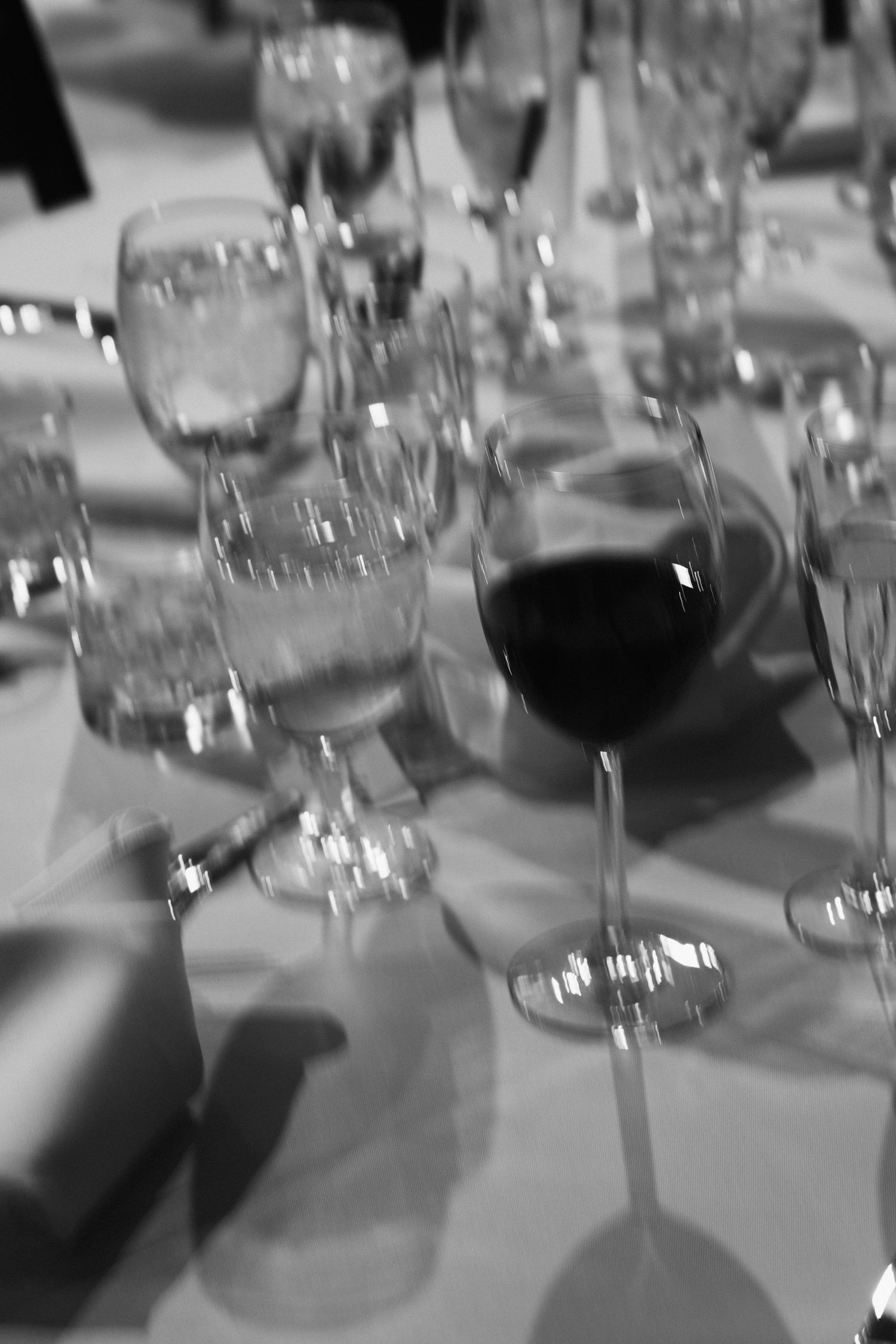 Black and white close-up of elegant crystal wine and water glasses on a wedding rehearsal table.