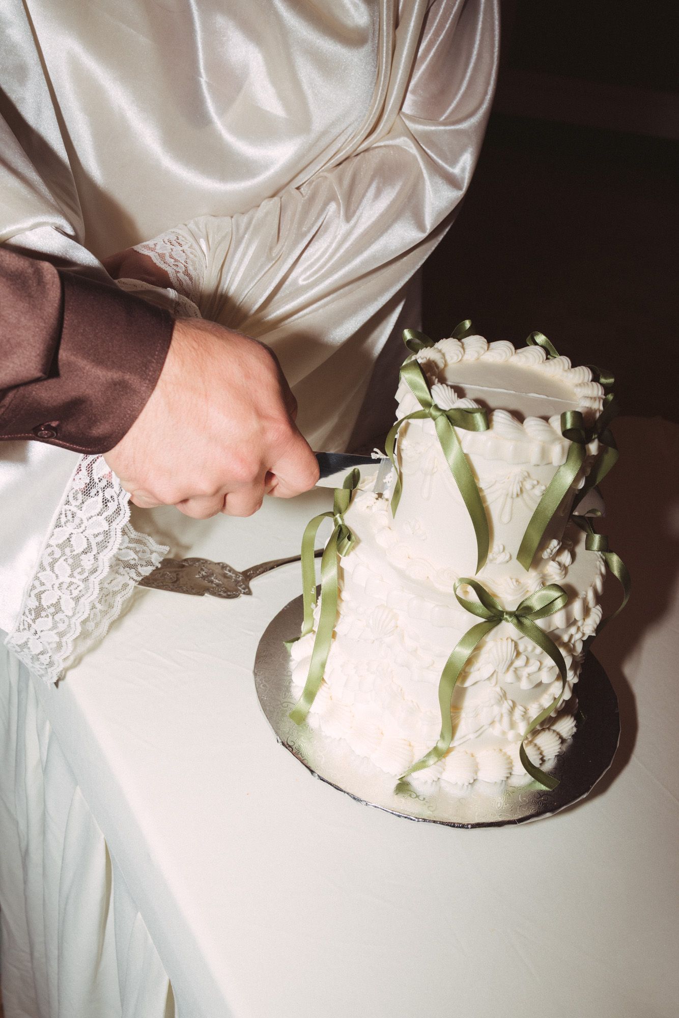 Bride and groom cutting a two-tier white wedding cake decorated with green ribbons and floral details.