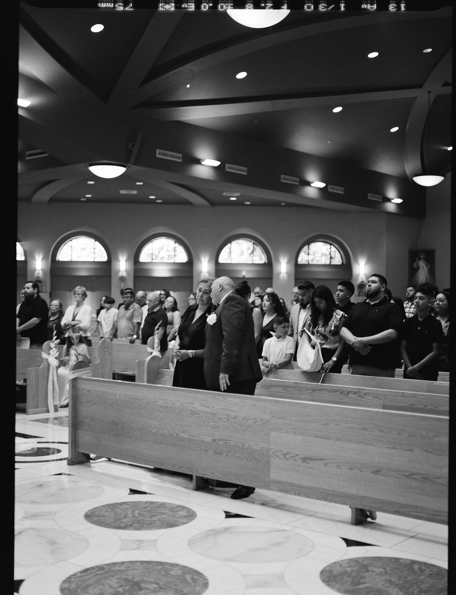 Wedding guests standing in church pews during a ceremony in a beautiful arched catholic church.