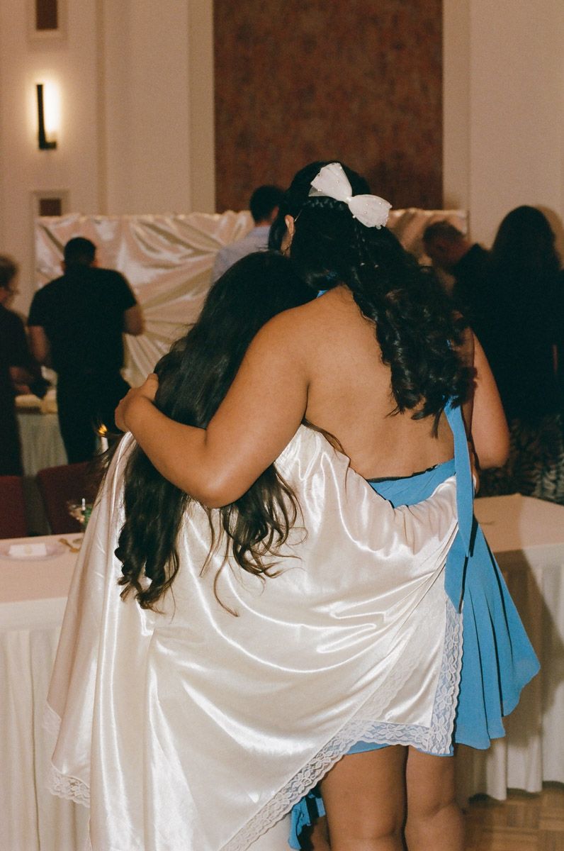 Bride embraces a guest at her wedding reception, hugging her from the side.
