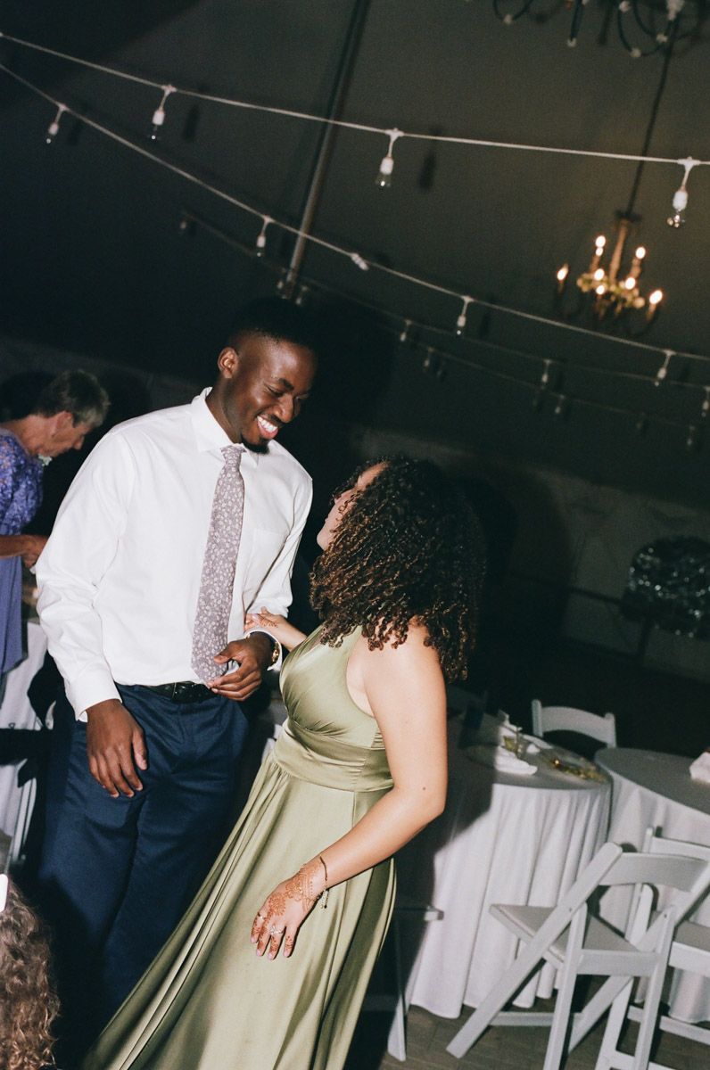 A couple shares a joyful dance at a wedding reception under string lights and a chandelier.
