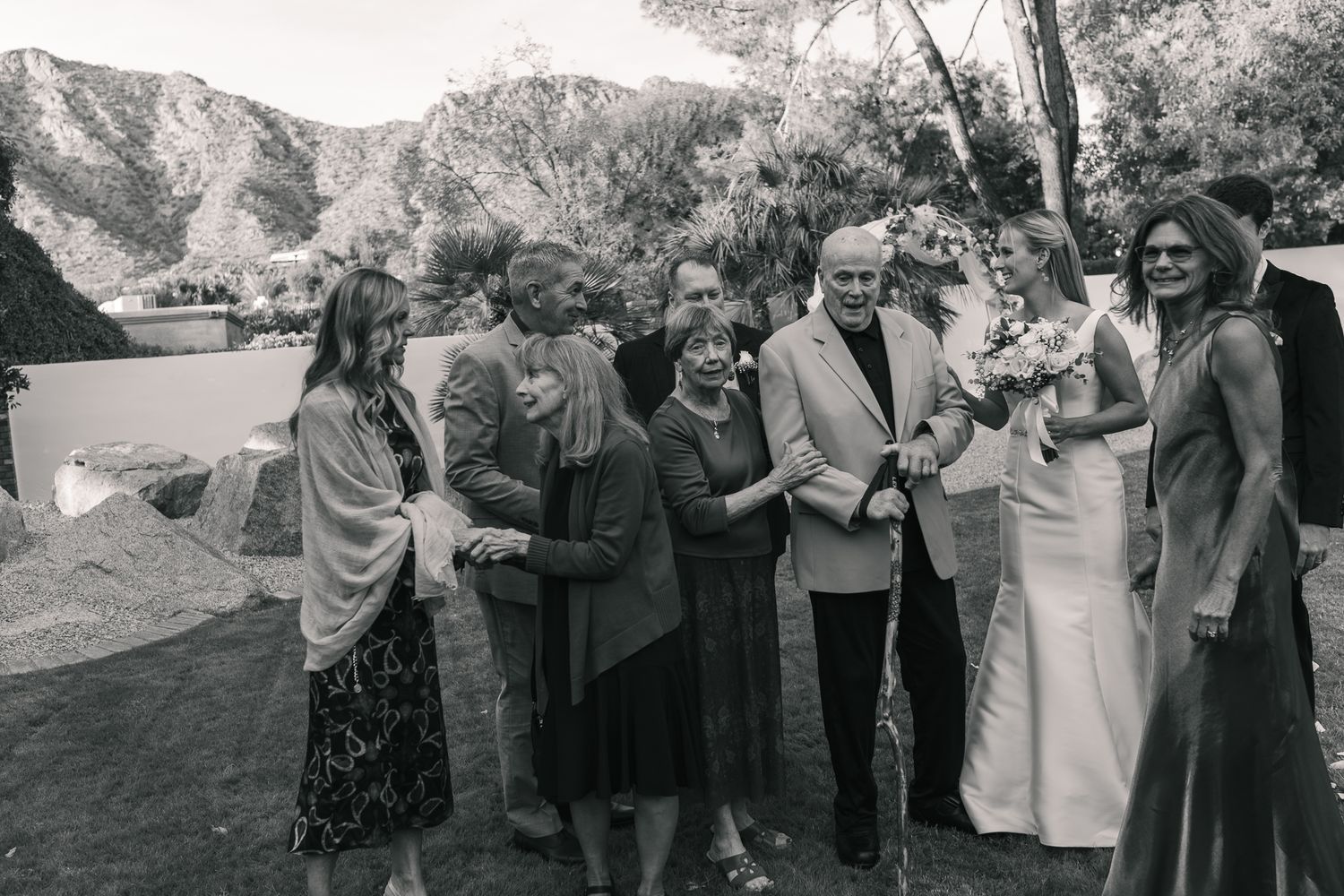 Black and white photo of bride with wedding party and family posing outdoors with mountain backdrop.