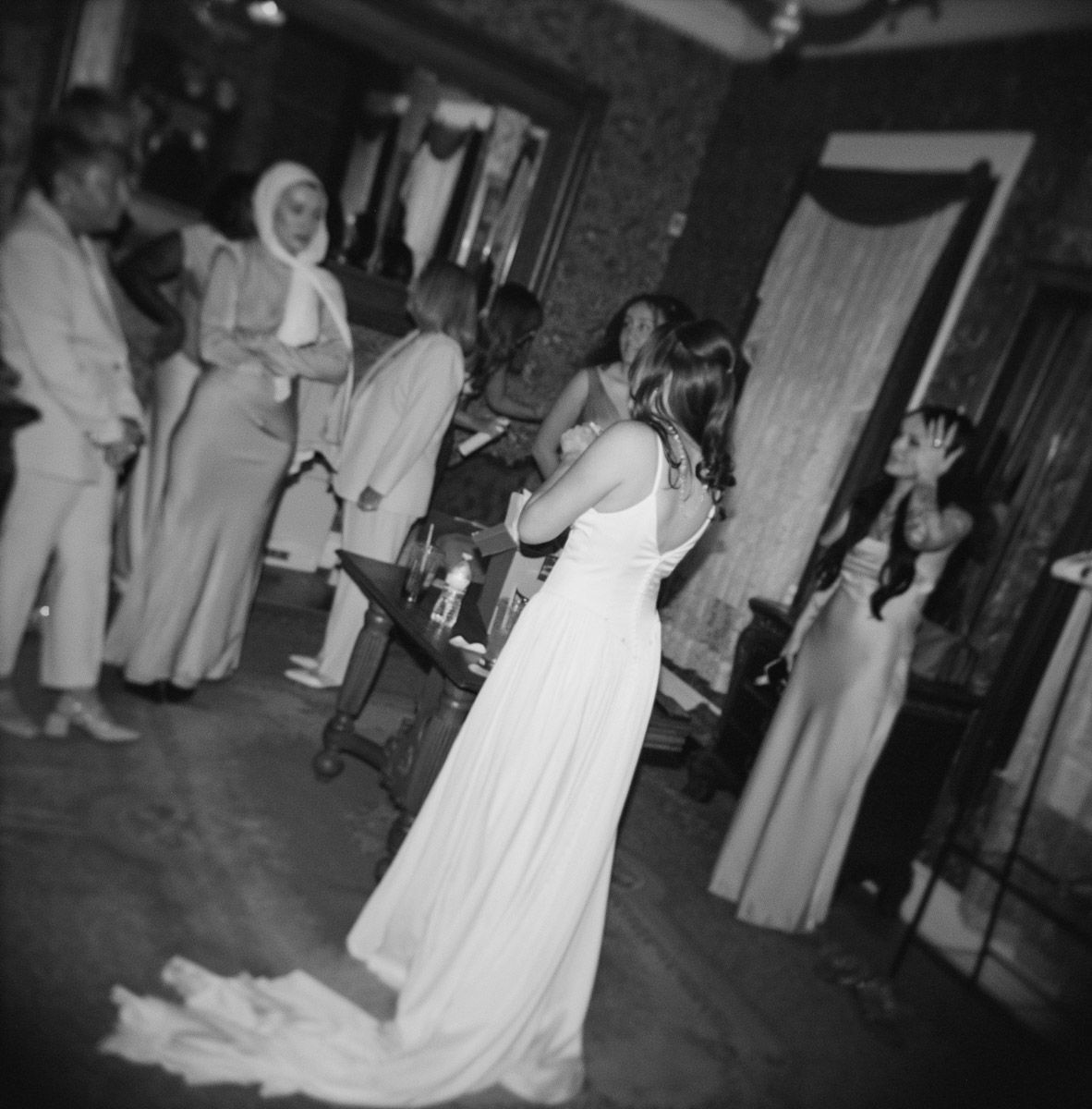 Black and white film photo of a bride in her wedding dress surrounded by bridesmaids in their getting ready room.