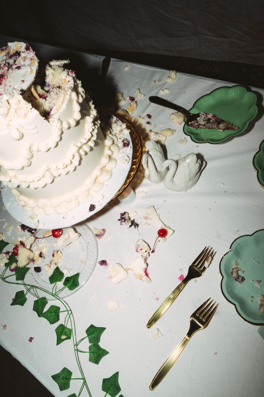 Two-tier white wedding cake with berry filling on decorated table with gold forks and green plates.