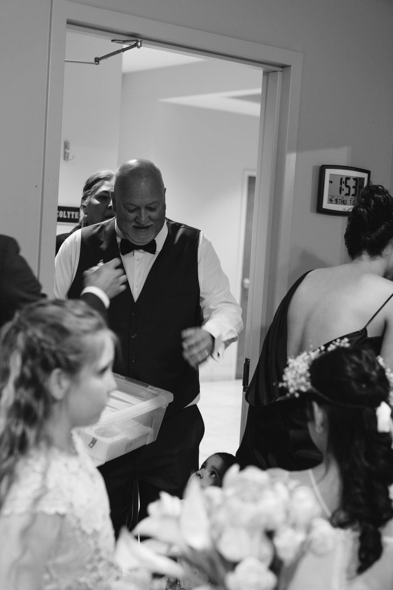 Black and white photo of father adjusting bow tie while surrounded by bridal party members.
