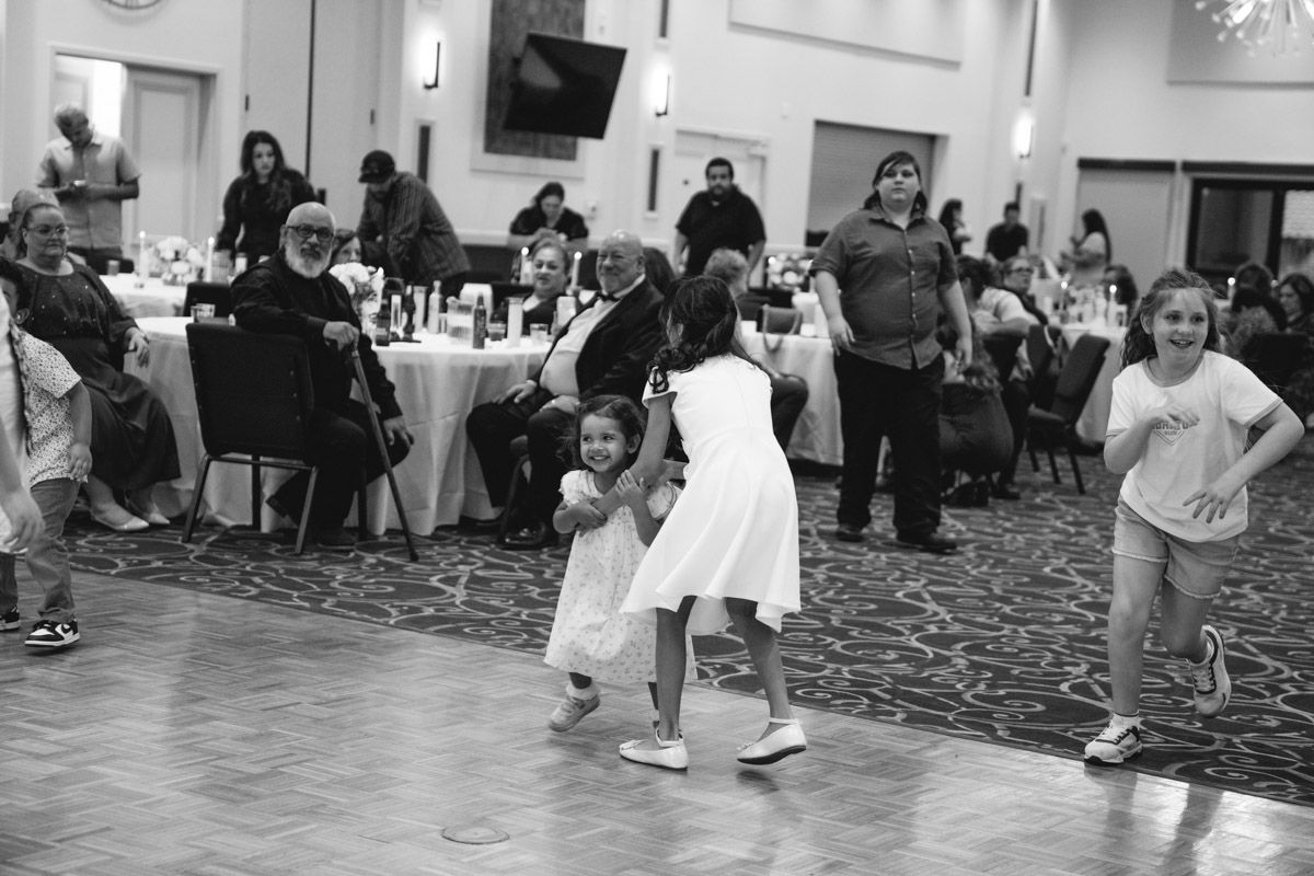 Children dancing joyfully at a wedding reception, black and white photo capturing candid family celebration moments.