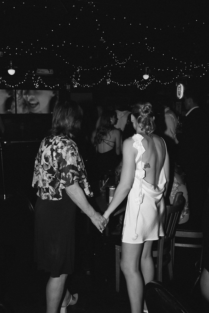 Black and white photo of two women holding hands at an elegant evening event with string lights.
