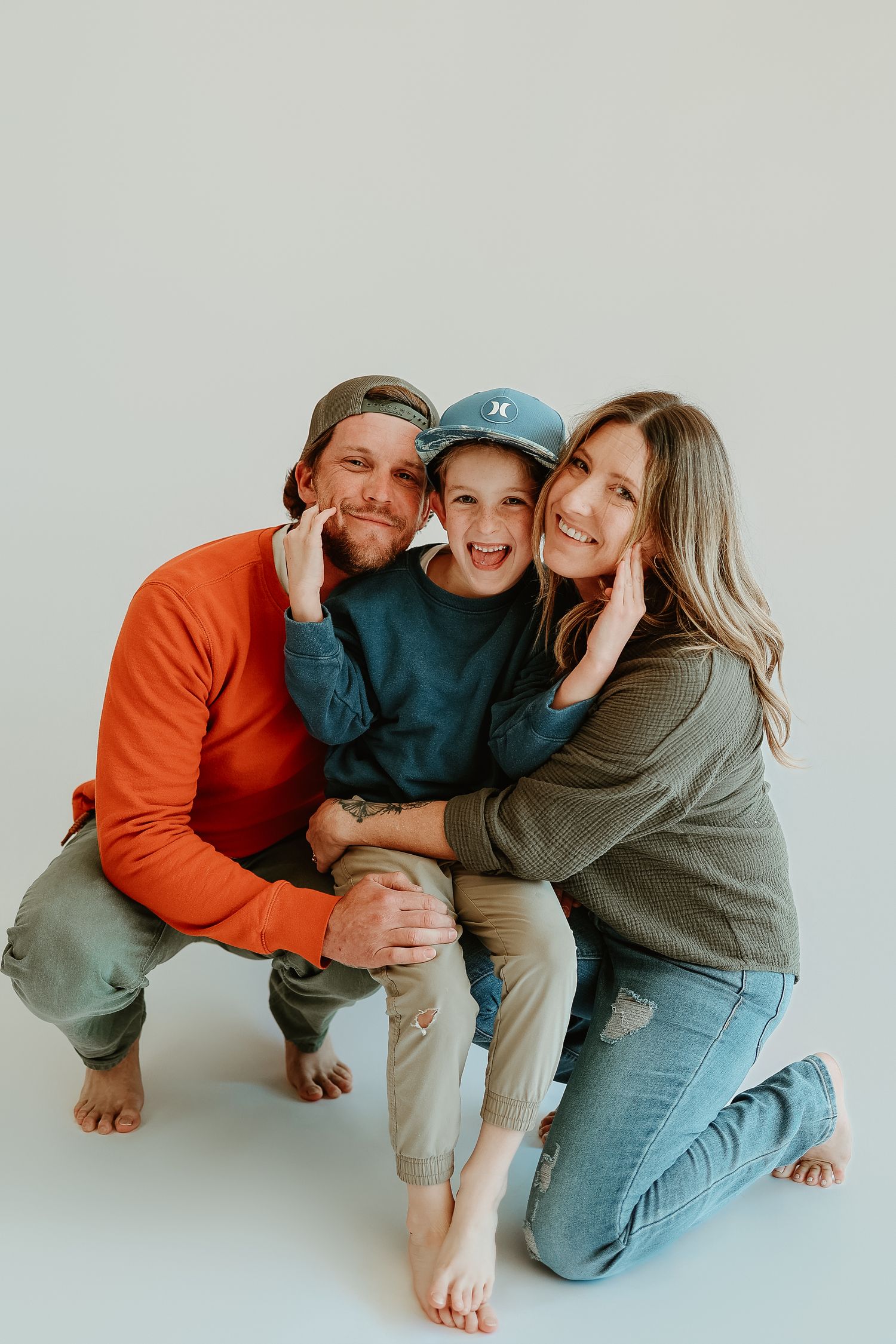 A happy family of three poses together on a white background, with parents hugging their smiling child.