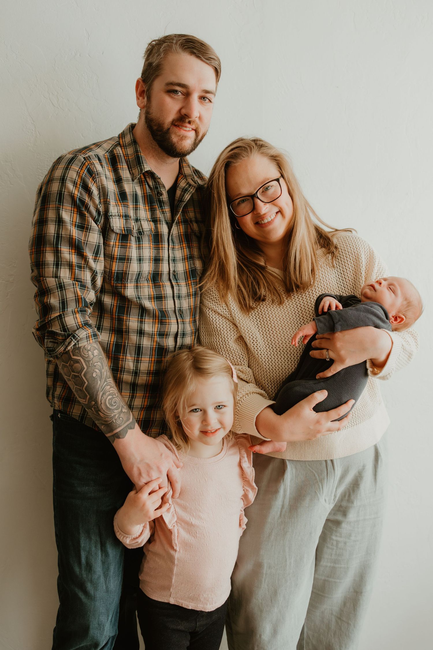 A family portrait in warm tones featuring two parents with a young child and an infant against a light background.