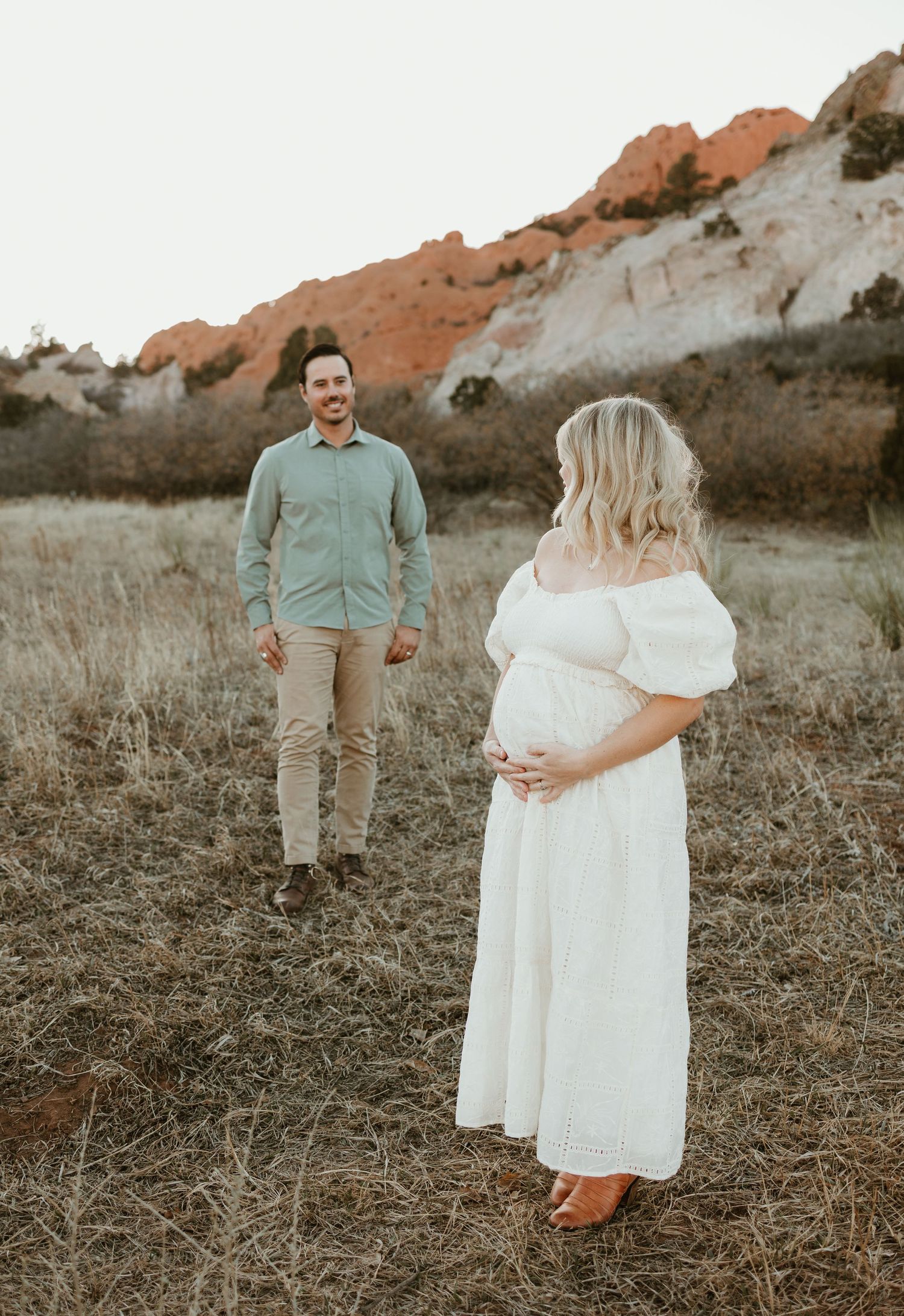 A couple poses in a field against red rock formations during a romantic maternity photo session at sunset.
