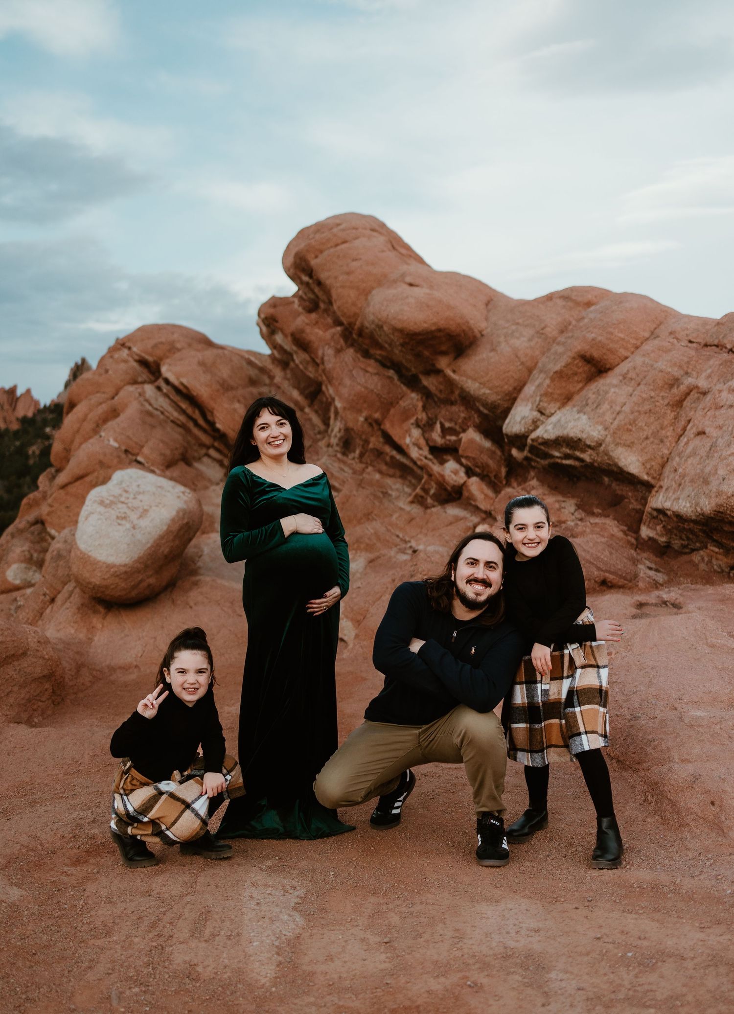 A group poses together against red rock formations at sunset wearing coordinated black and plaid outfits.