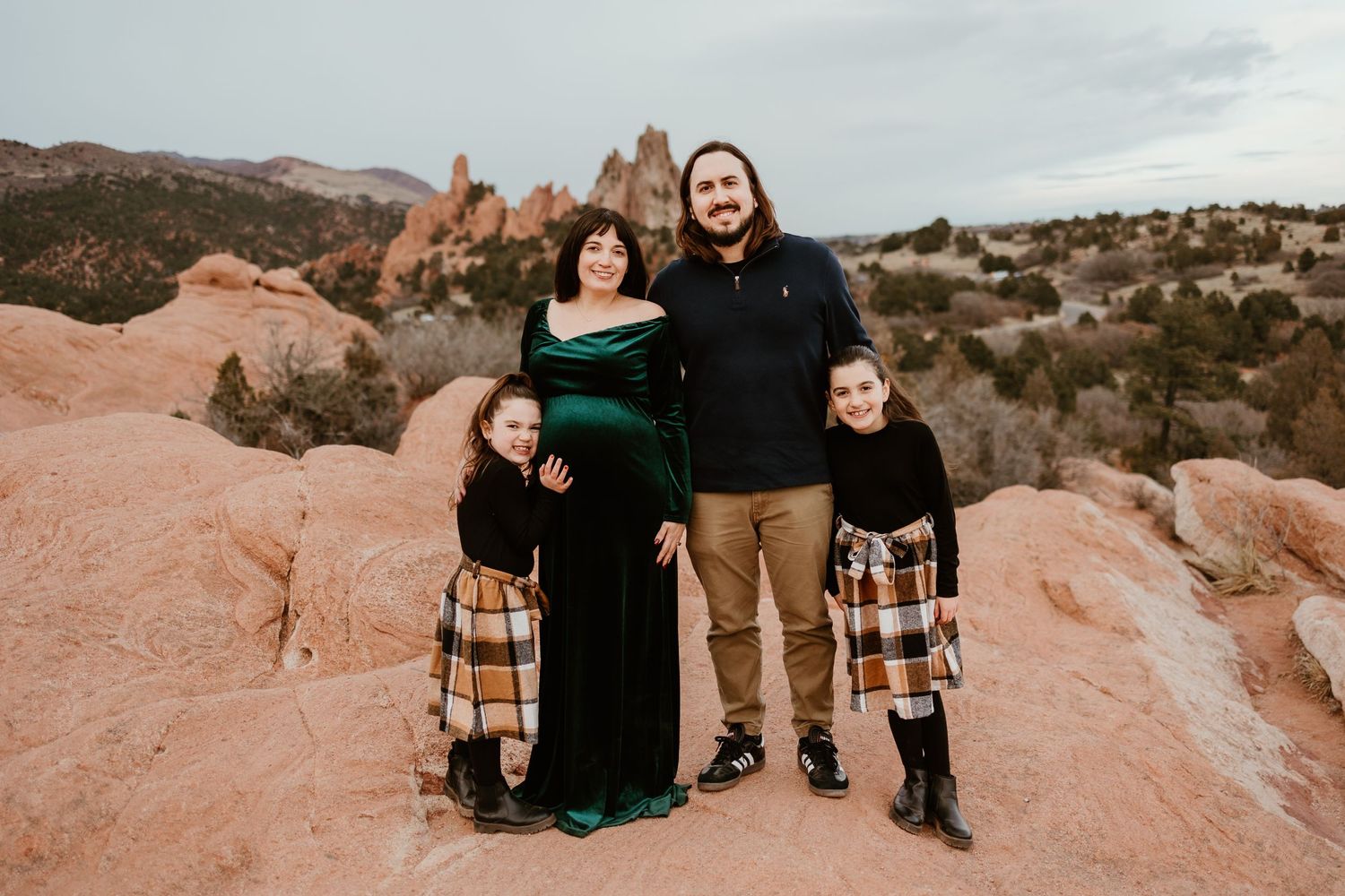 A family poses together on red rocks at Garden of the Gods park in Colorado during sunset.