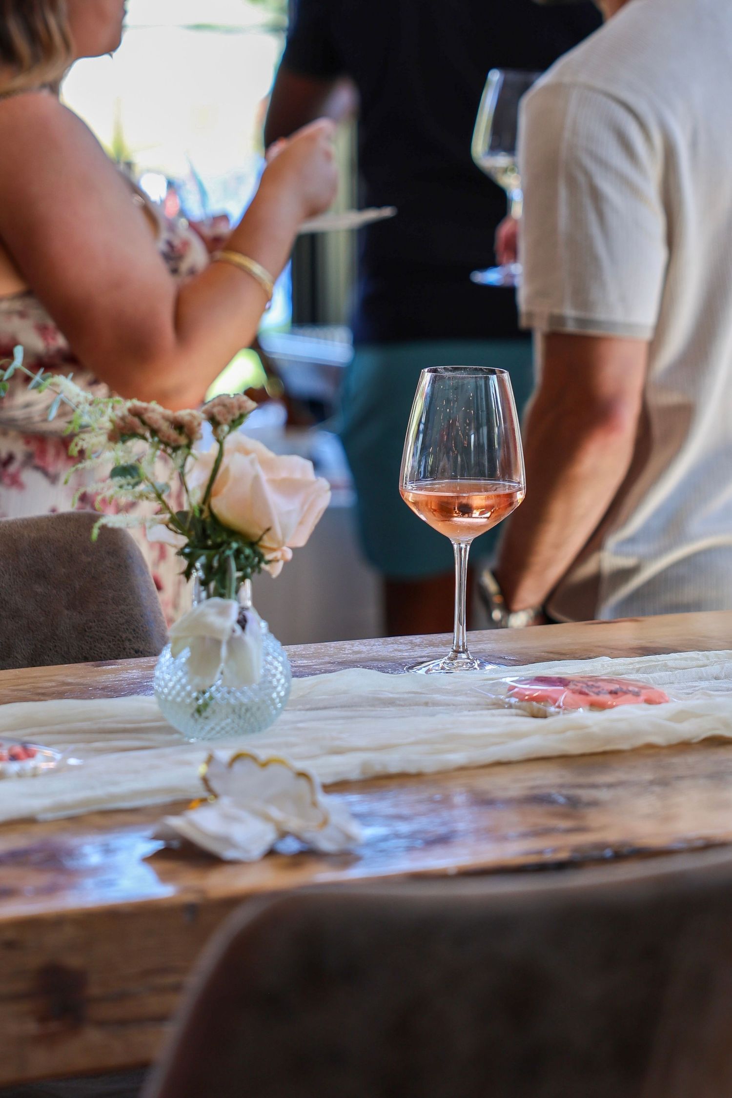 Glass of rose wine on a rustic wooden table with floral centerpiece at an elegant party.