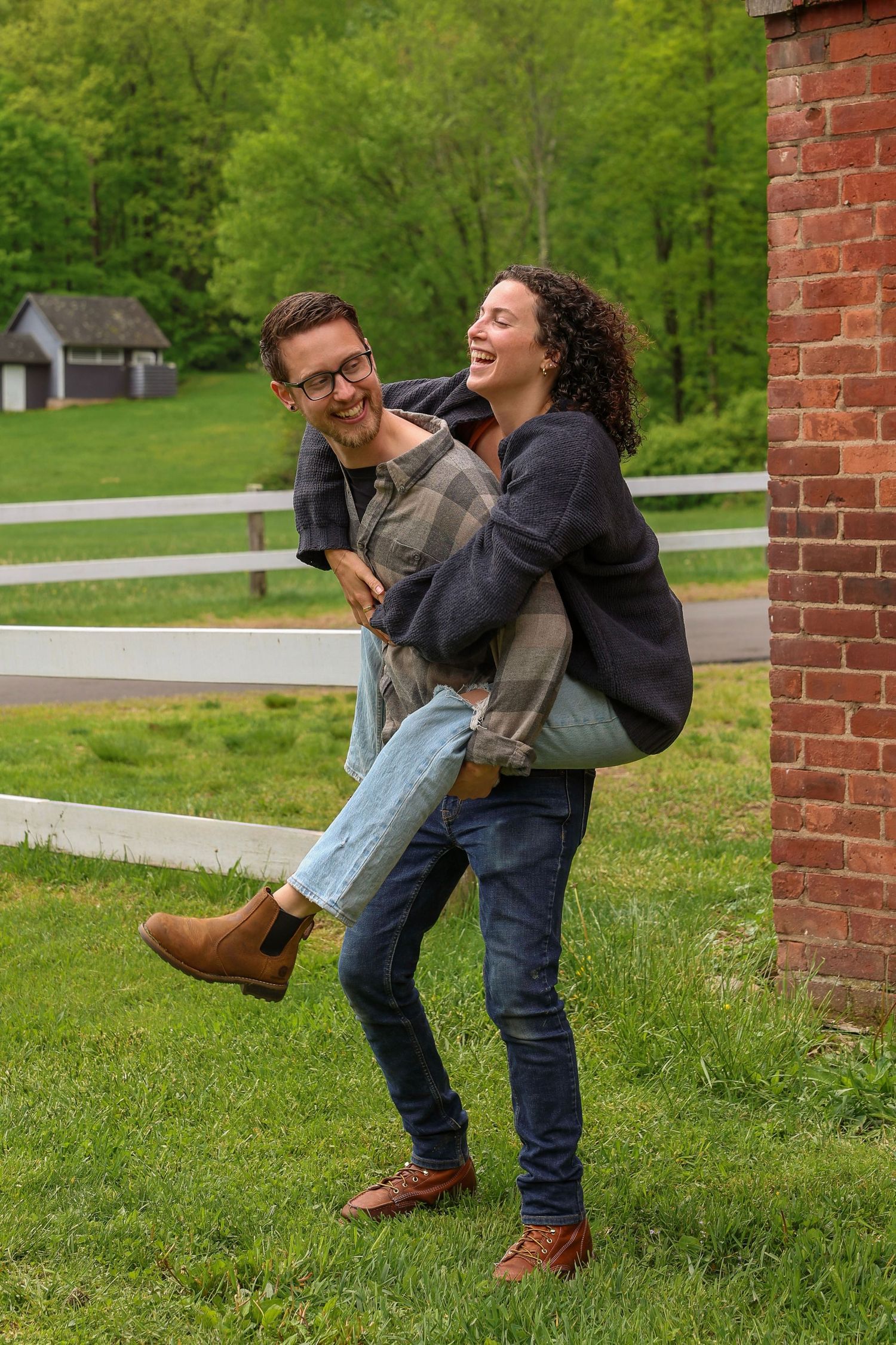 A joyful couple laughing as the man carries the woman in his arms near a brick building outdoors.